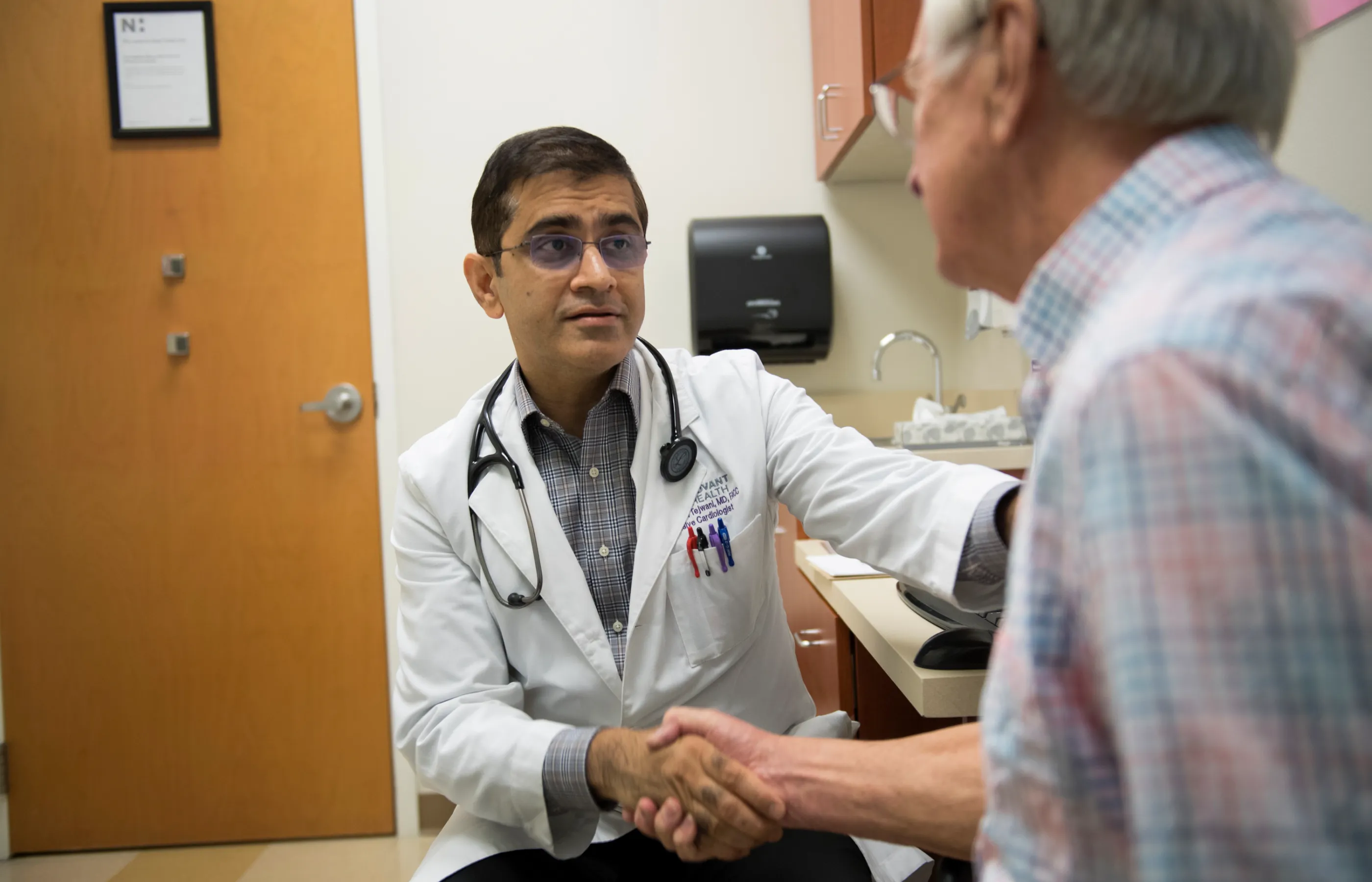 Dr. Tejwani is sitting across from a senior male patient in exam room. The two are shaking hands. 