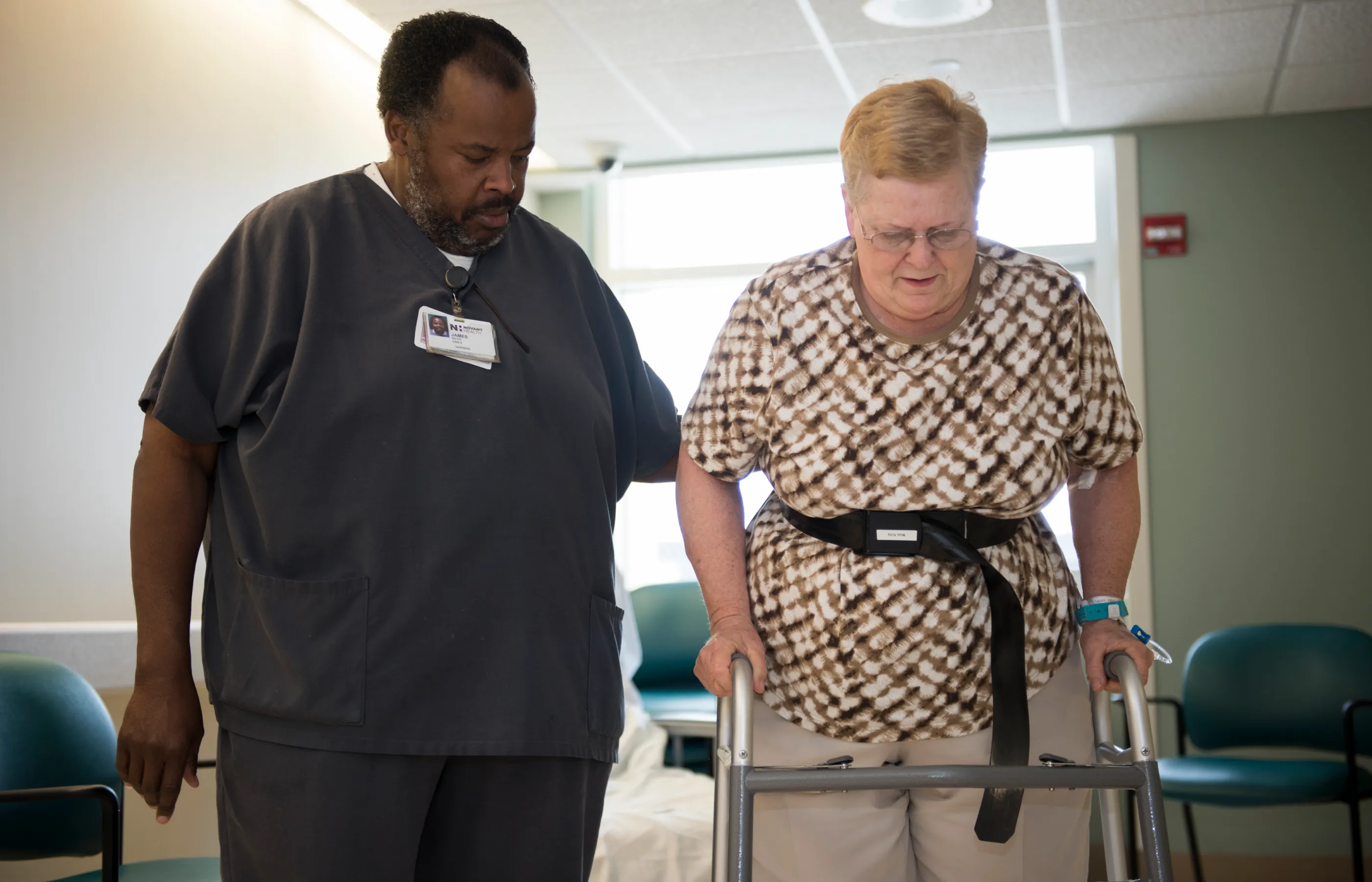 A male nurse is assistant a patient as she walks with a walker A male nurse is assistant a patient as she walks with a walker