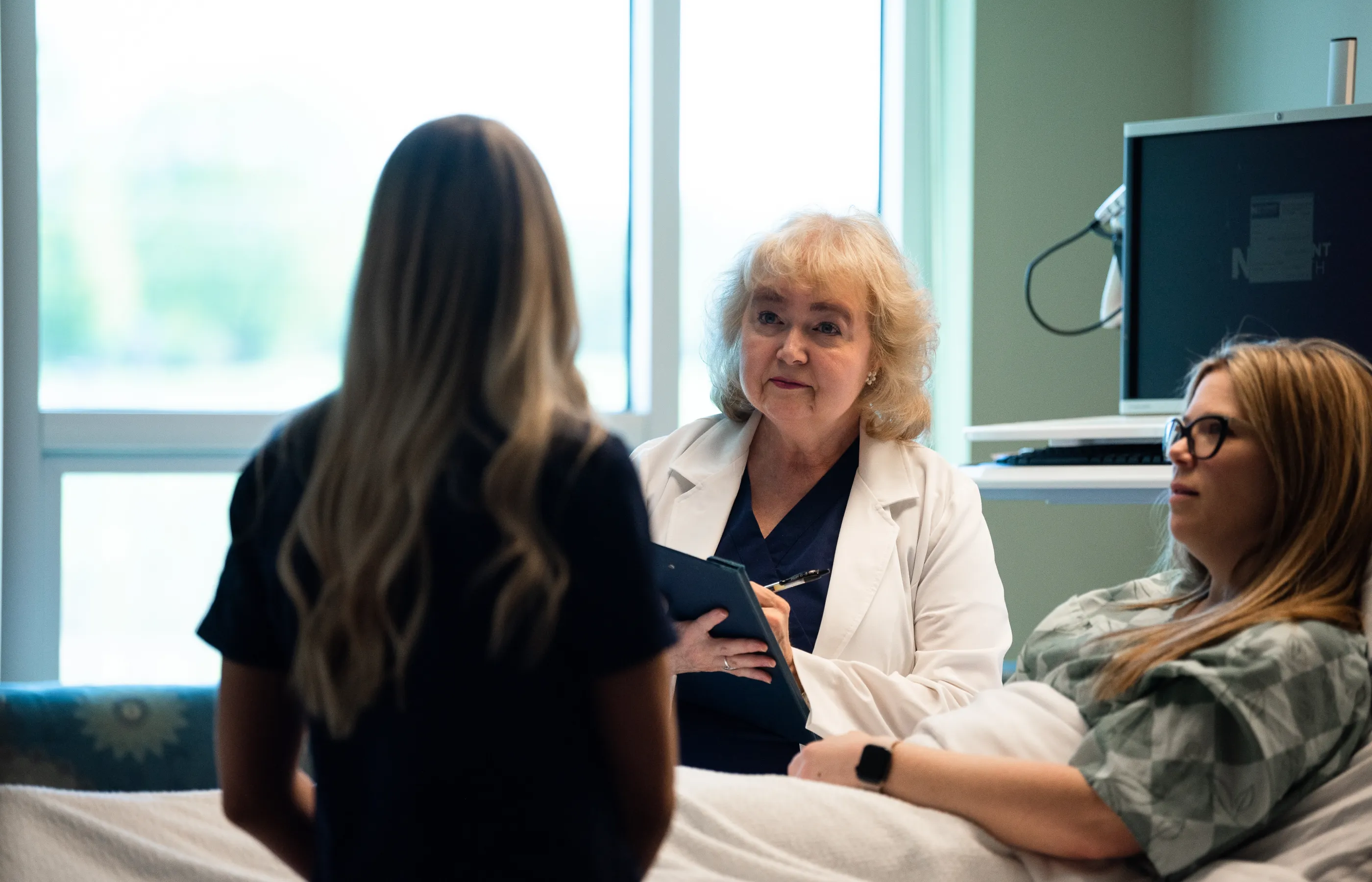 A Novant Health doctor and nurse are standing at a patient's bedside documenting and discussing treatment. 