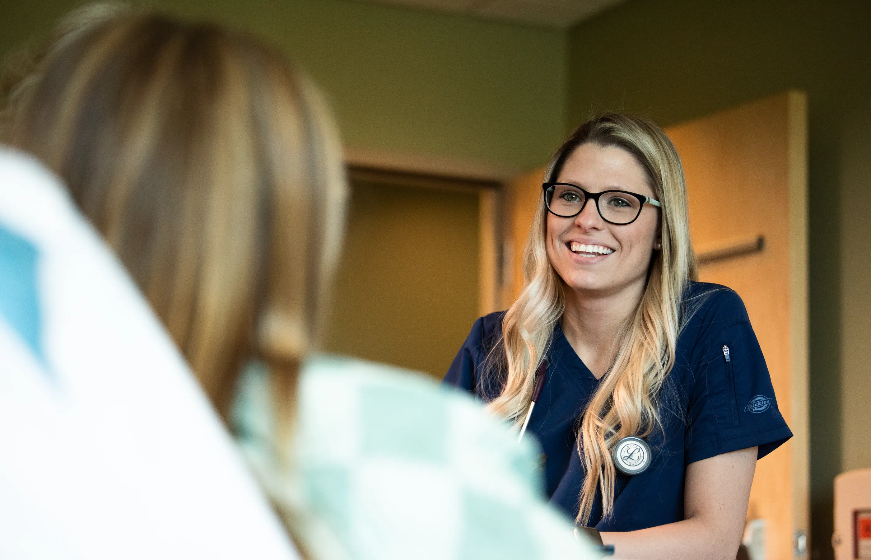 A Novant Health nurse is talking and smiling with a patient as they lie in a hospital bed. 