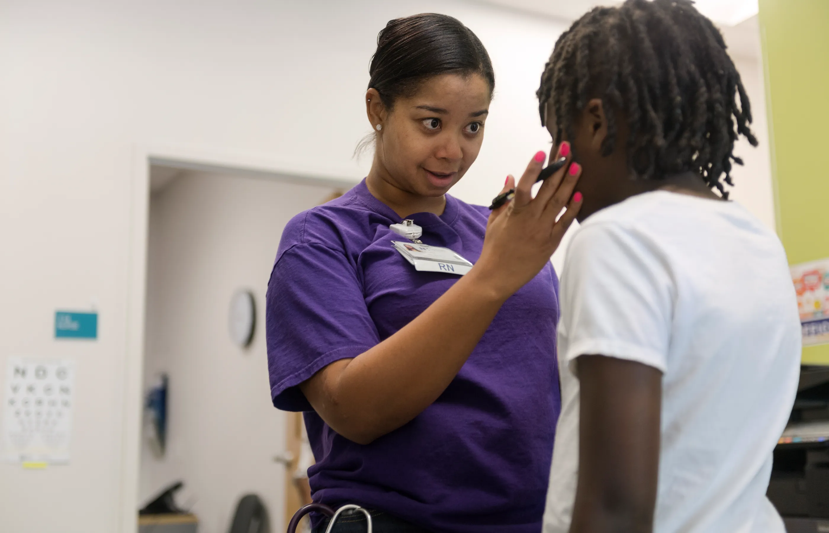 A Novant Health Registered Nurse (RN) is talking with a young child. The RN has a hand placed on the childs face as she talks and looks them in the eye. 