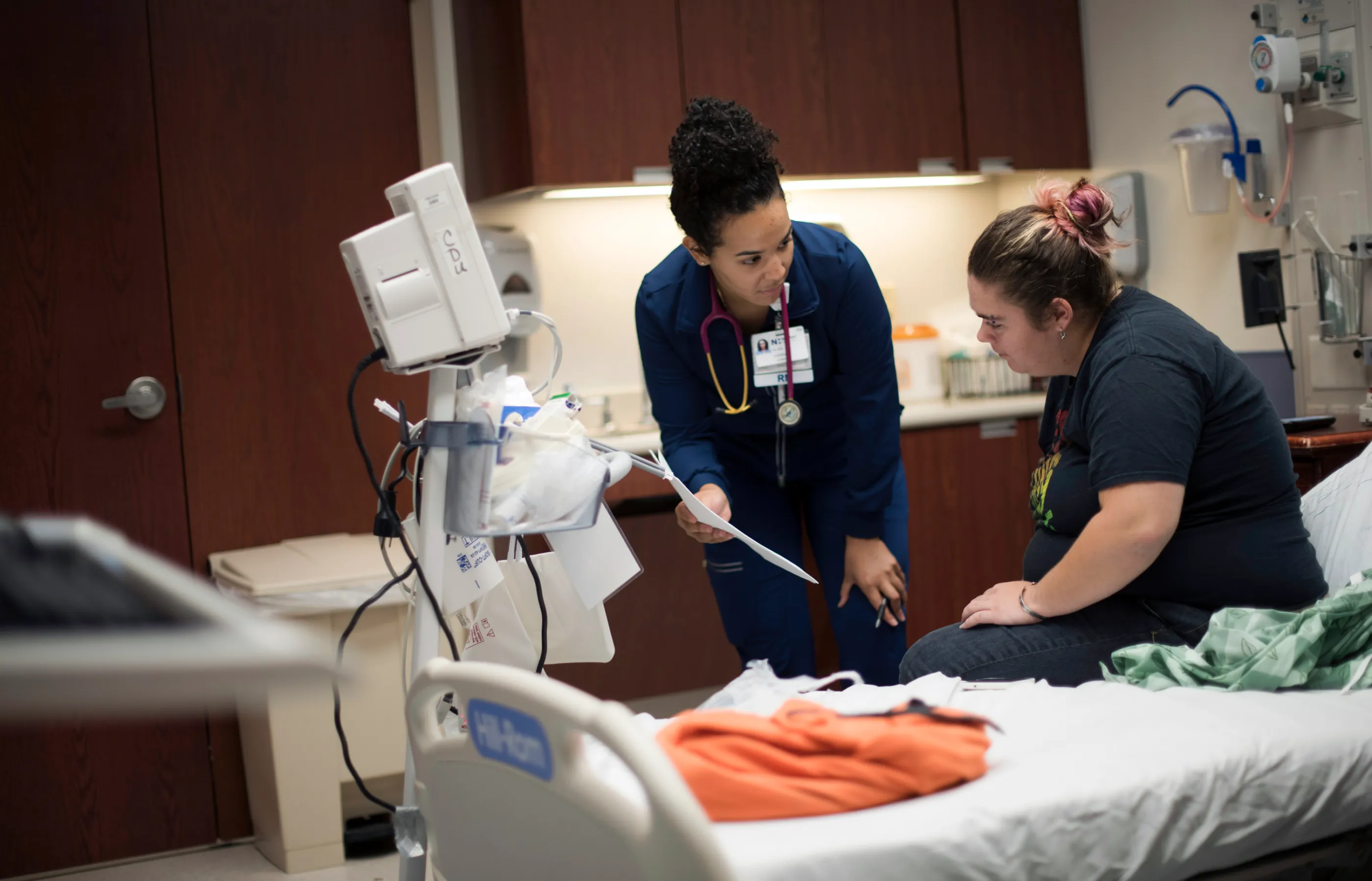  A patient is sitting on a hospital be while A Novant Health registered nurse shows the patient paperwork. 