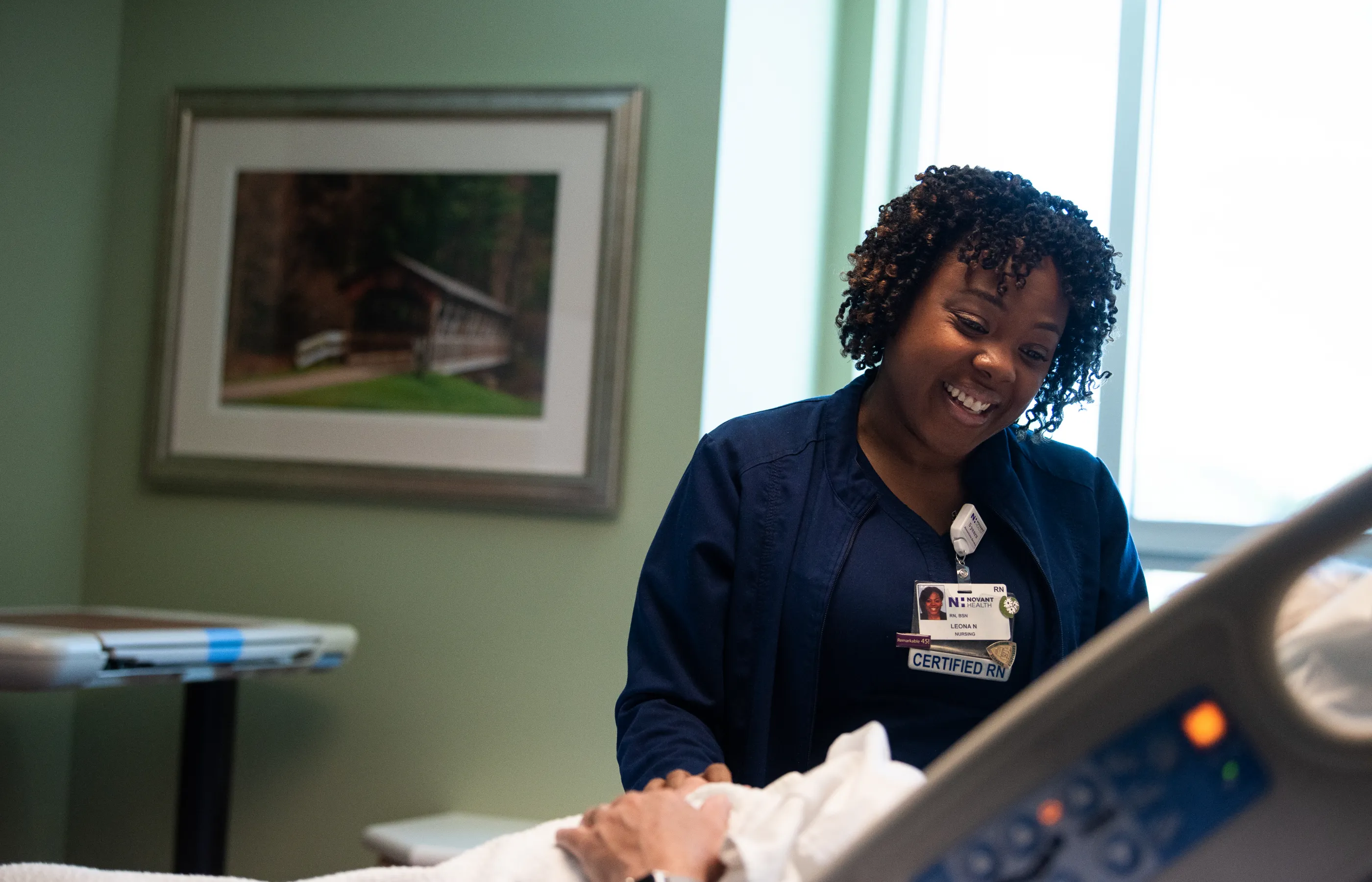 A Novant Health nurse is standing at the bedside of a patient.
