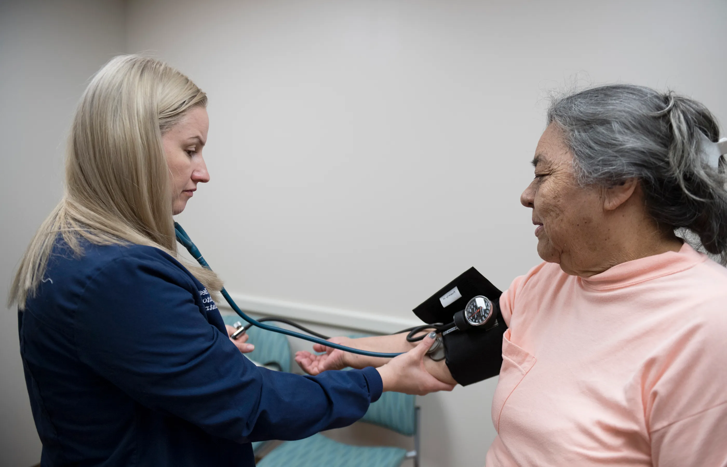 A Novant Health nurse is taking the blood pressure of a senior woman as she sits on an exam table. 