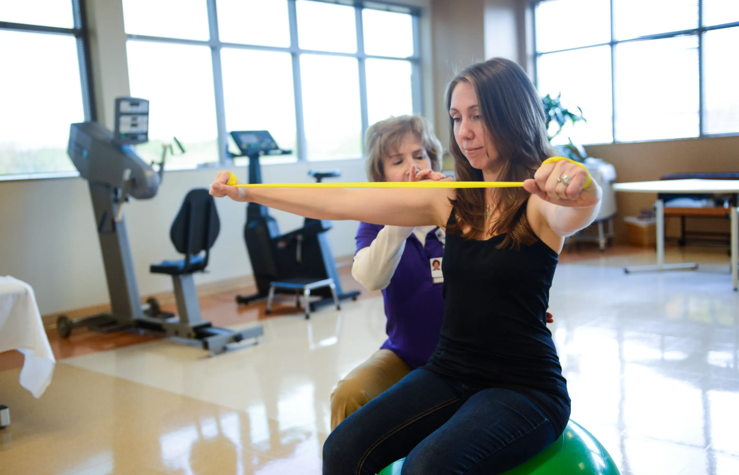 A physical therapist is guiding a woman as she completes exercises. 