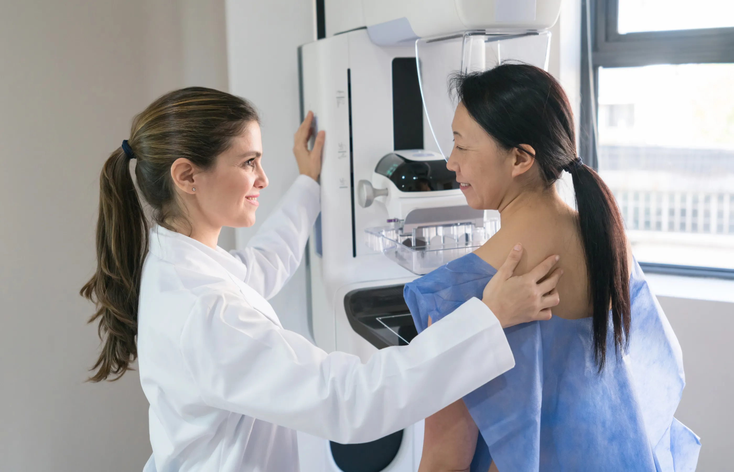 A healthcare provider is talking to and guiding a patient as she is preparing for a mammogram. 