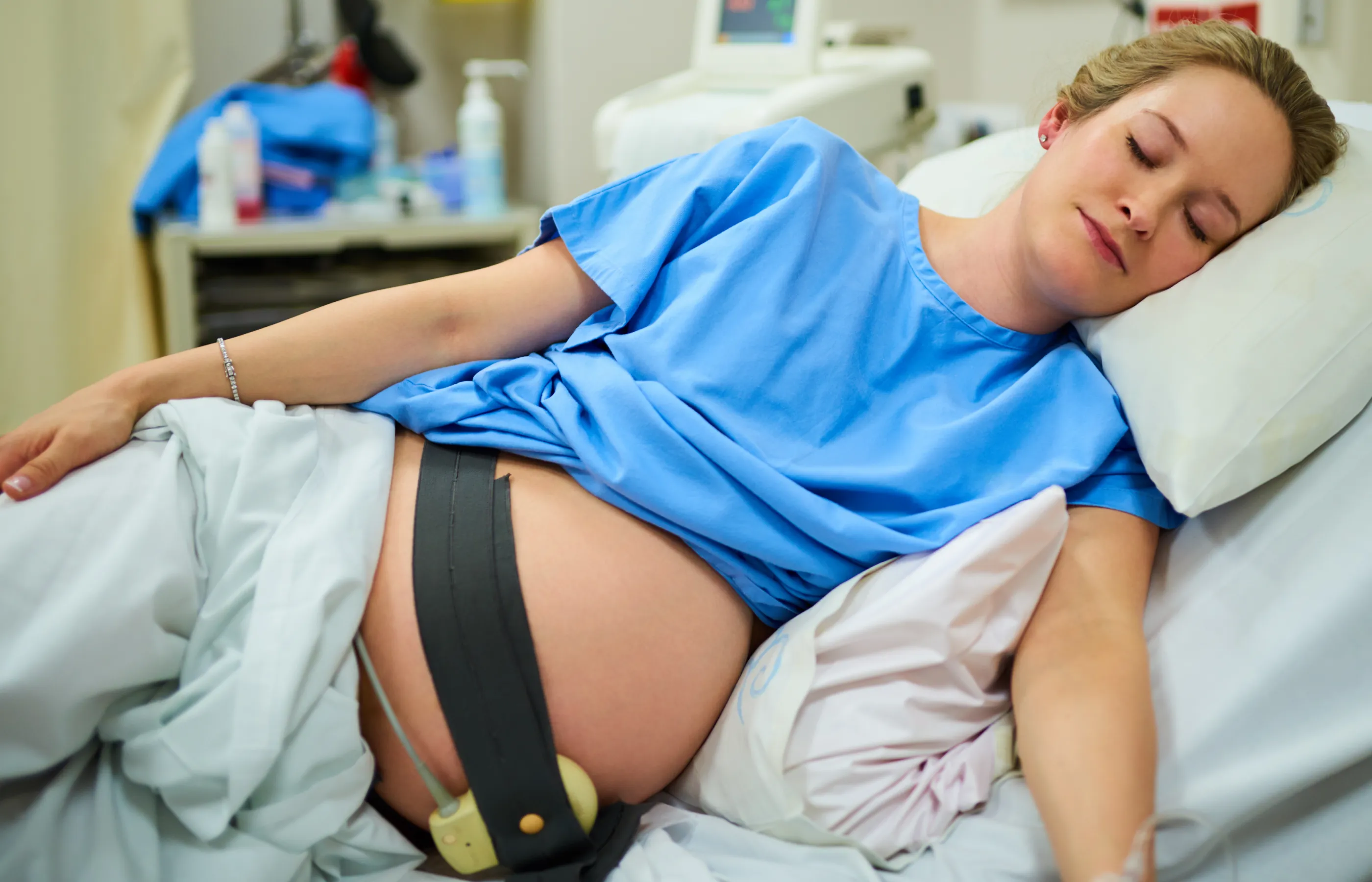 Woman is lying in a hospital bed with monitor straps on as she prepares for birth. 