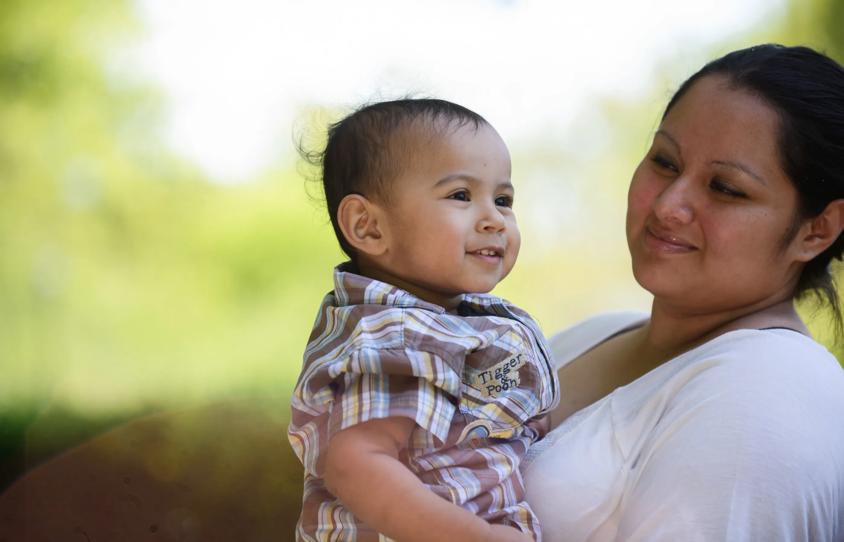 A mother is holding her toddler and smiling at him. 