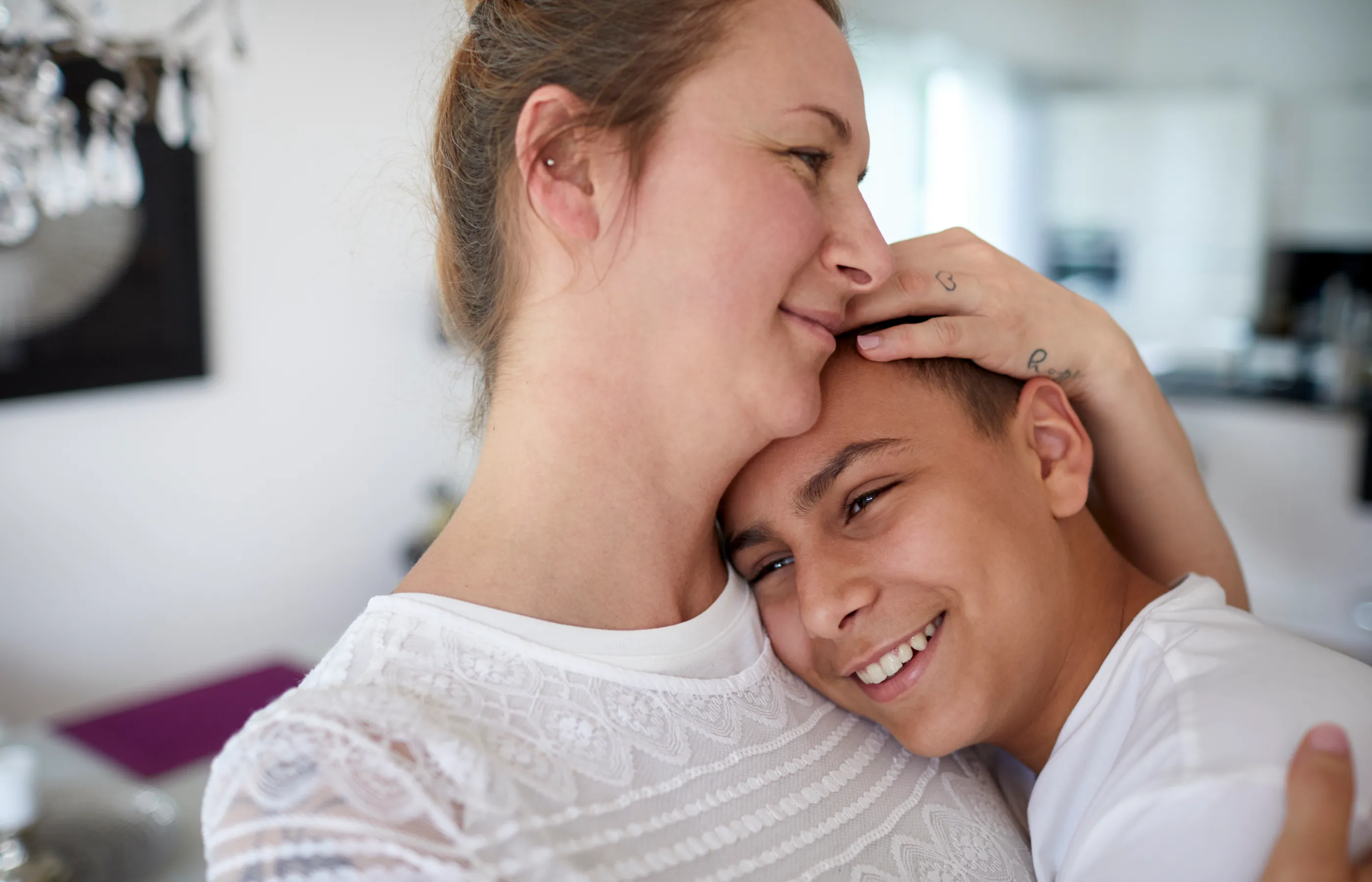 A teenage boy is resting his head on his mothers shoulder as she nestles him. 