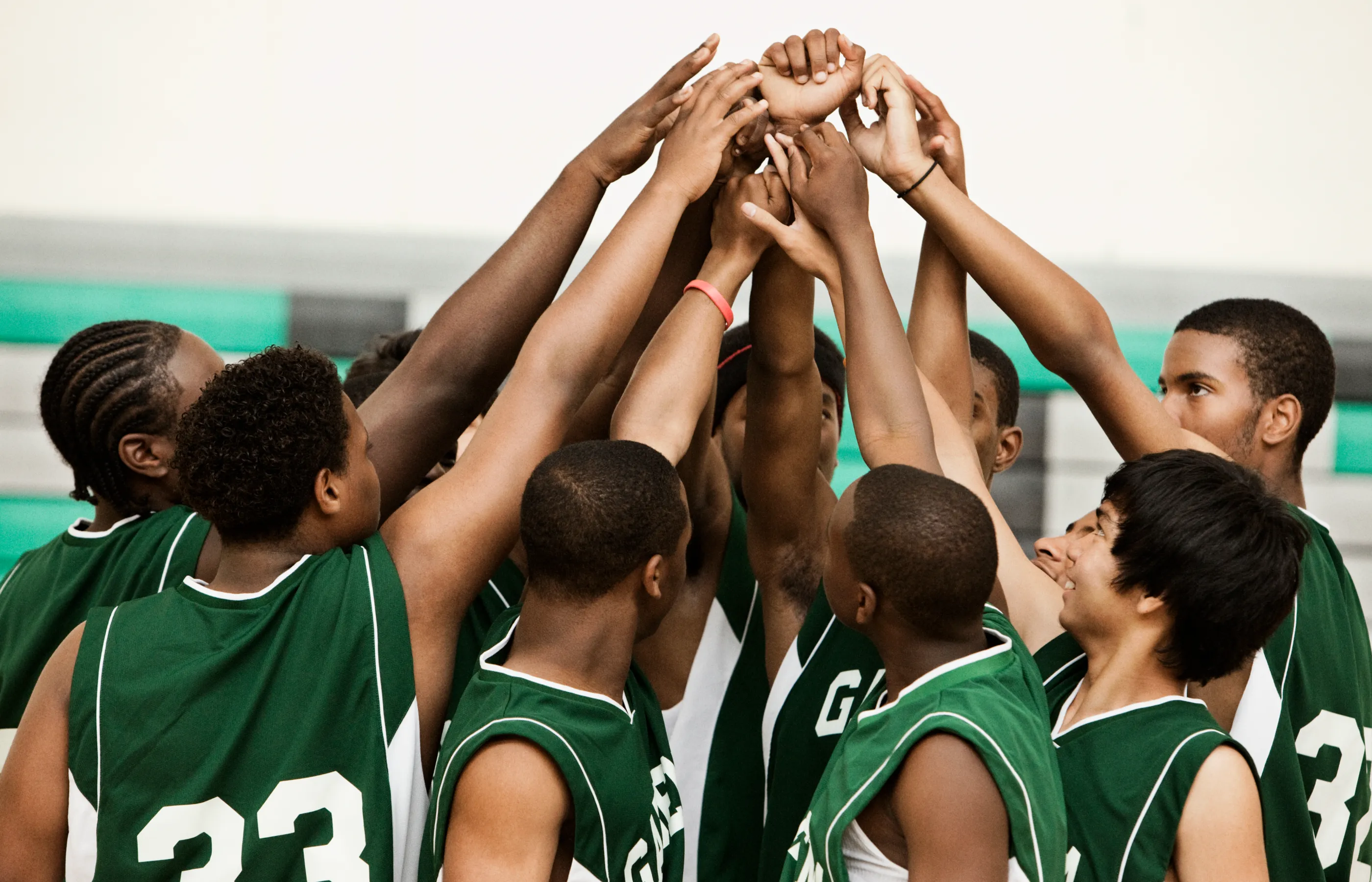 A young boys basketball team are huddled together with their hands in the air. 