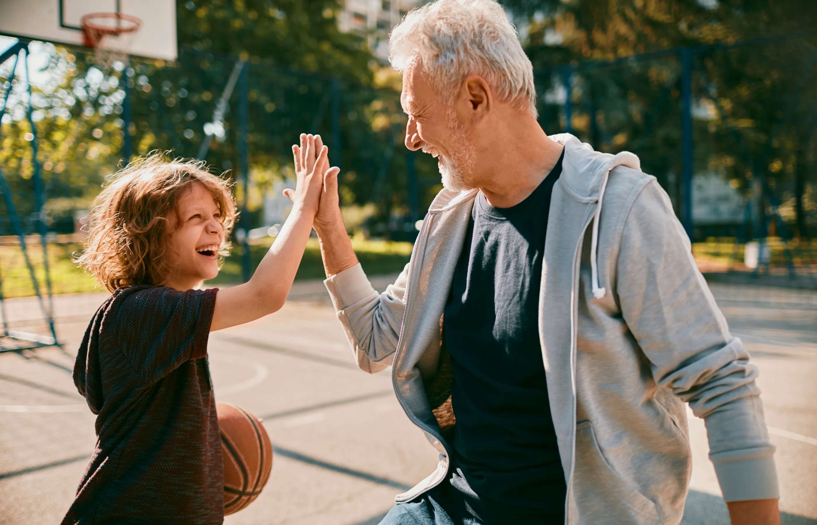A young child is outside playing basketball with his grandfather. 