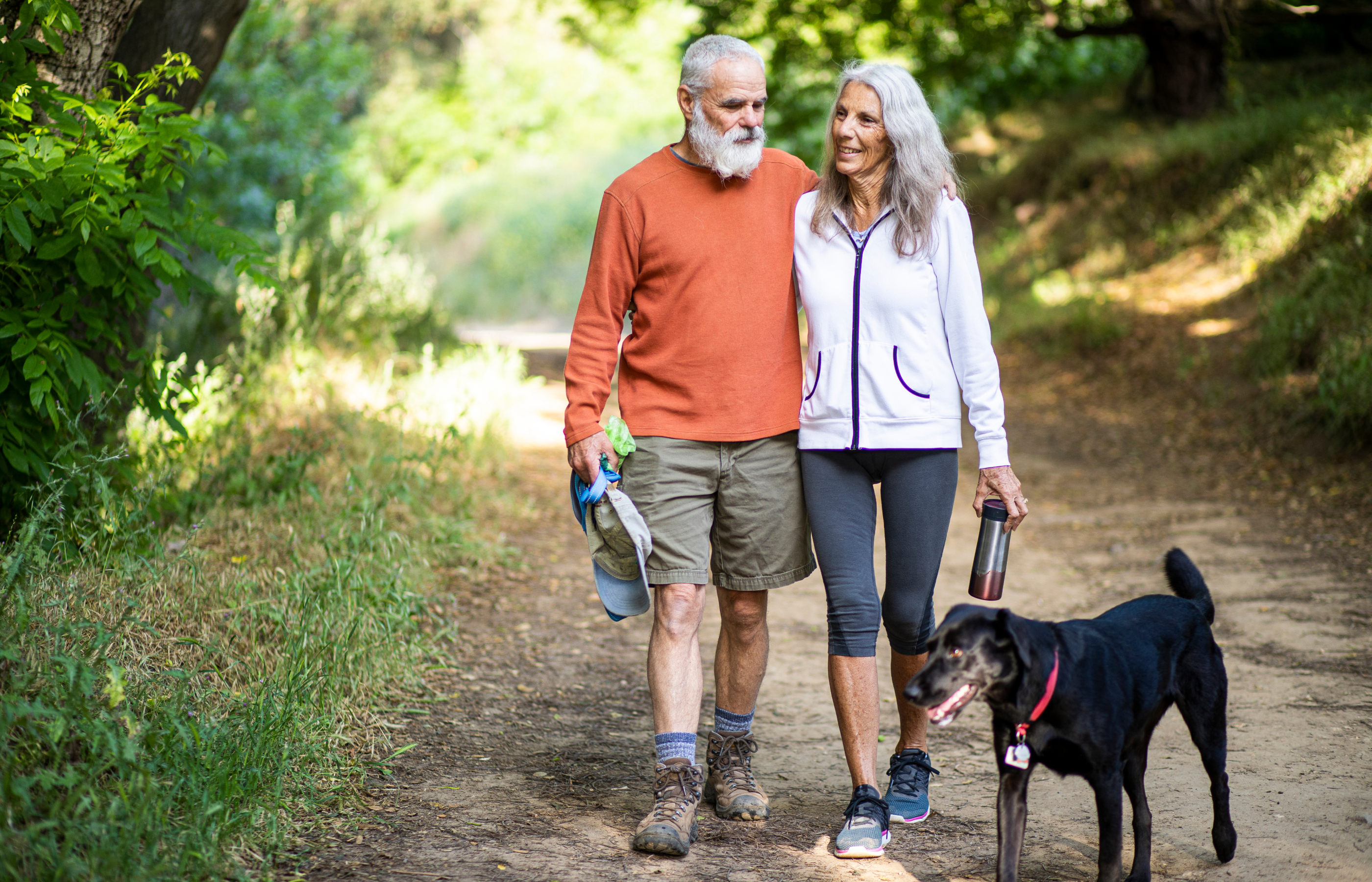 A man, a woman and a dog walking on a trail outdoors. A man, a woman and a dog walking on a trail outdoors.