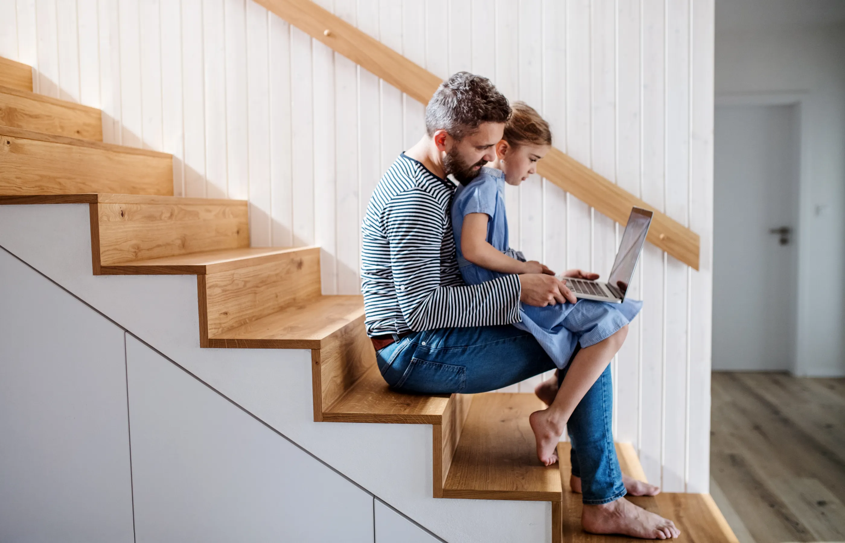 Father sitting with child on their home staircase looking at a laptop computer. Father sitting with child on their home staircase looking at a laptop computer.