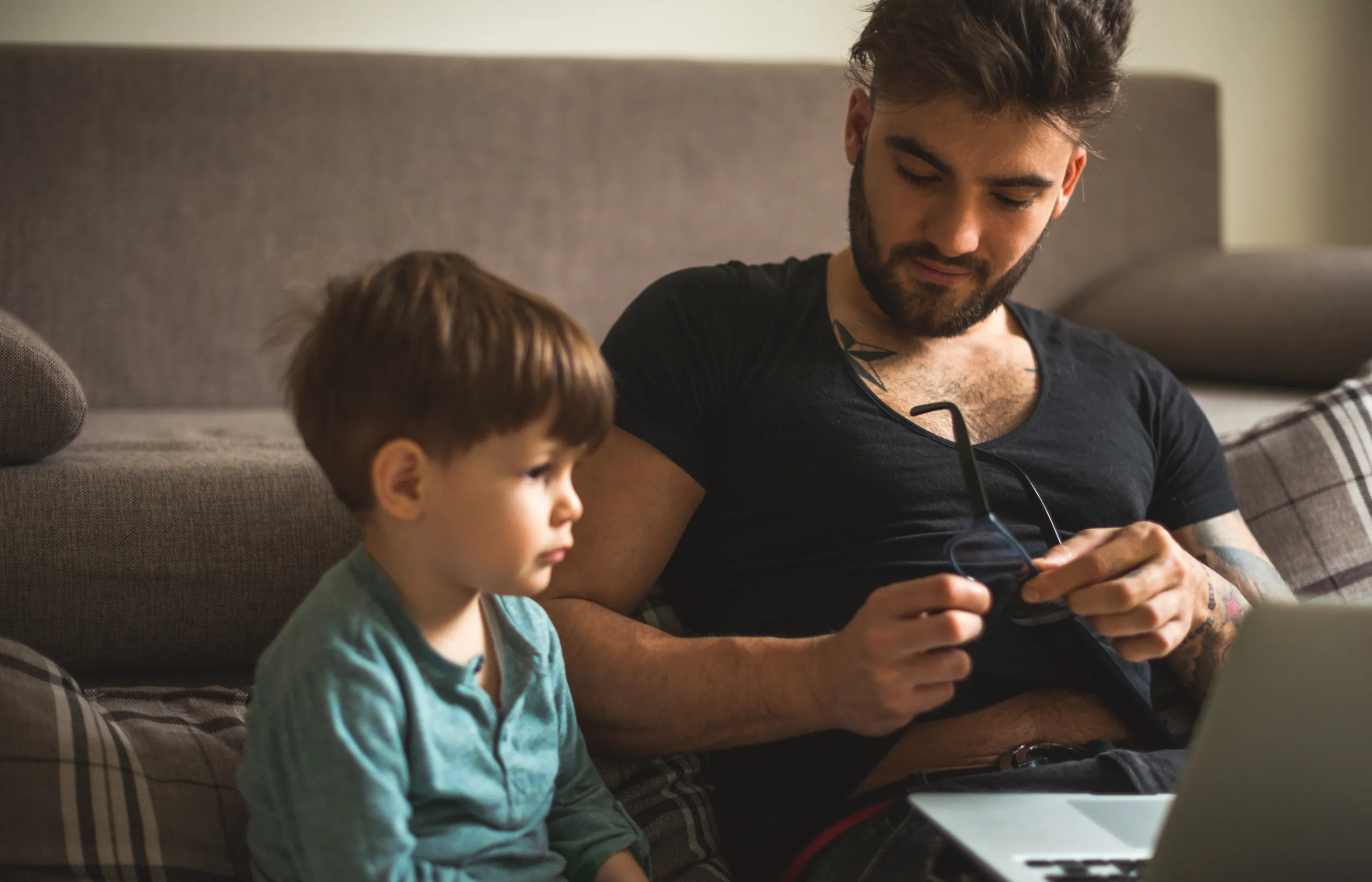 Man cleaning eyeglasses while watching cartoons with his boy