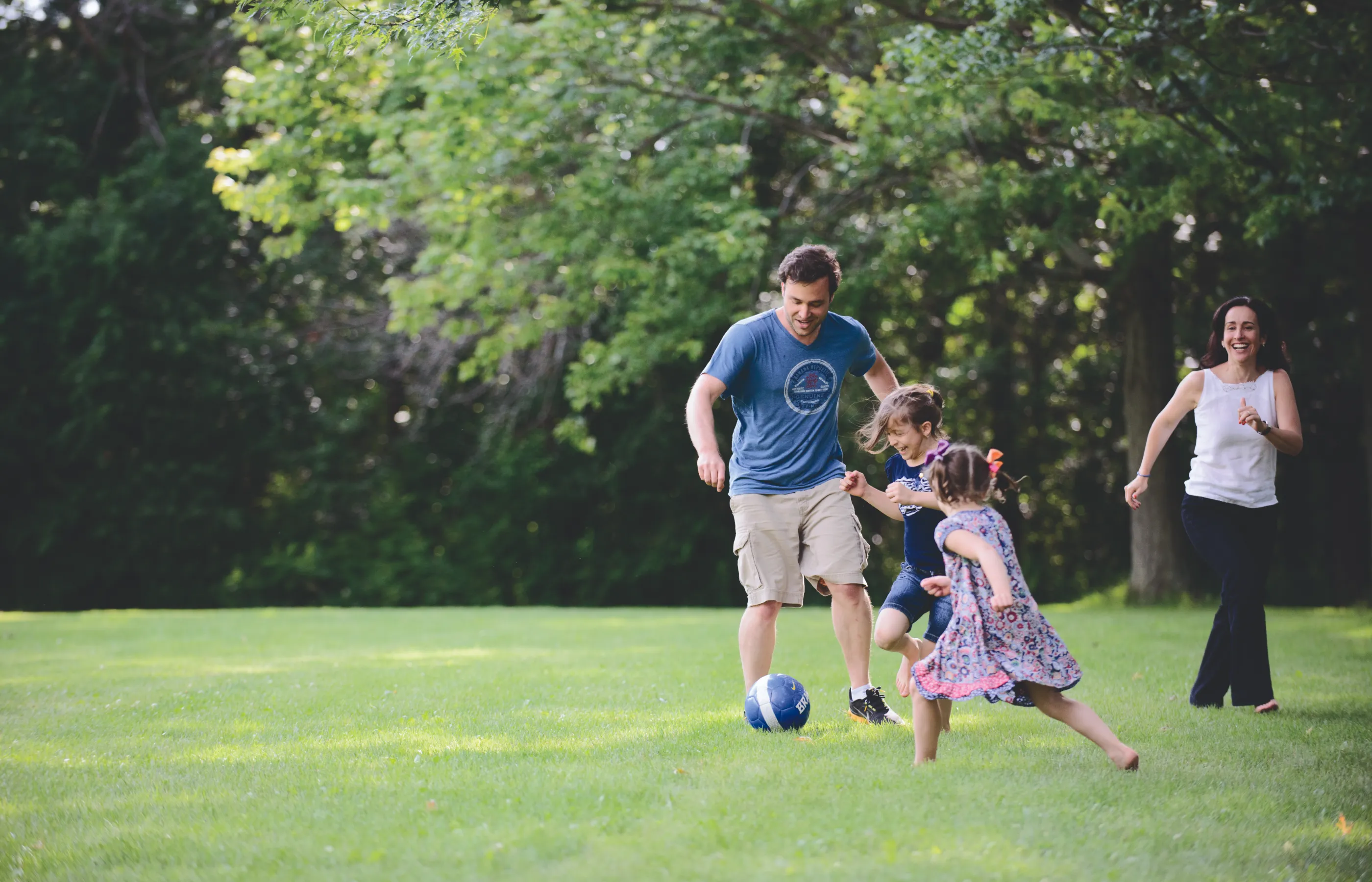 A family of four is outside running and playing with a soccer ball. 