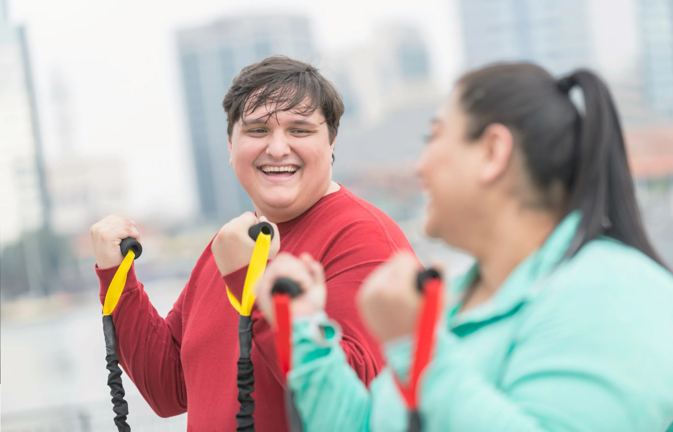 Two friends are smiling at one another as they work out with exercise bands. 