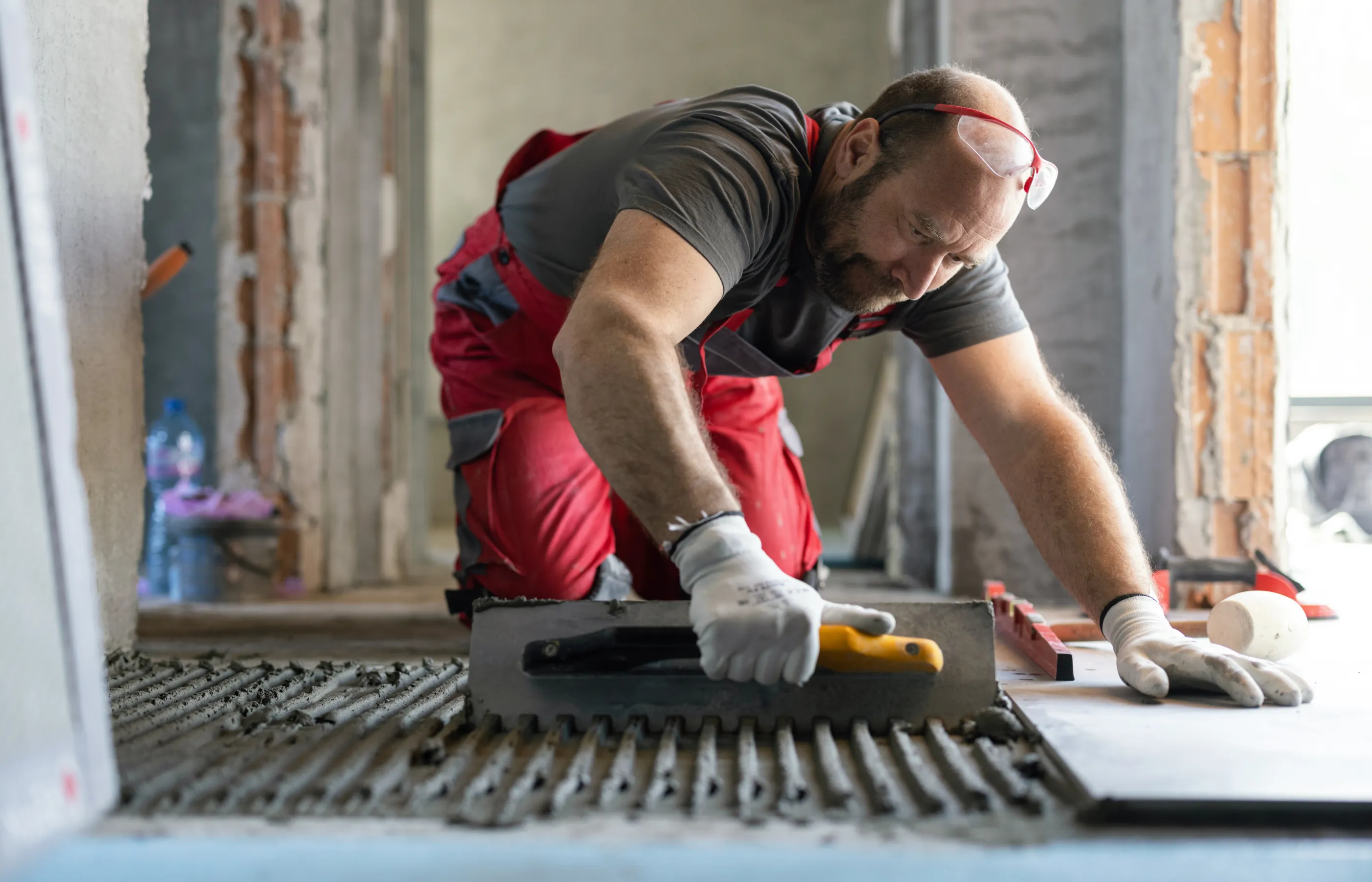 A man is kneeling down to install tile on the floor of a home. 