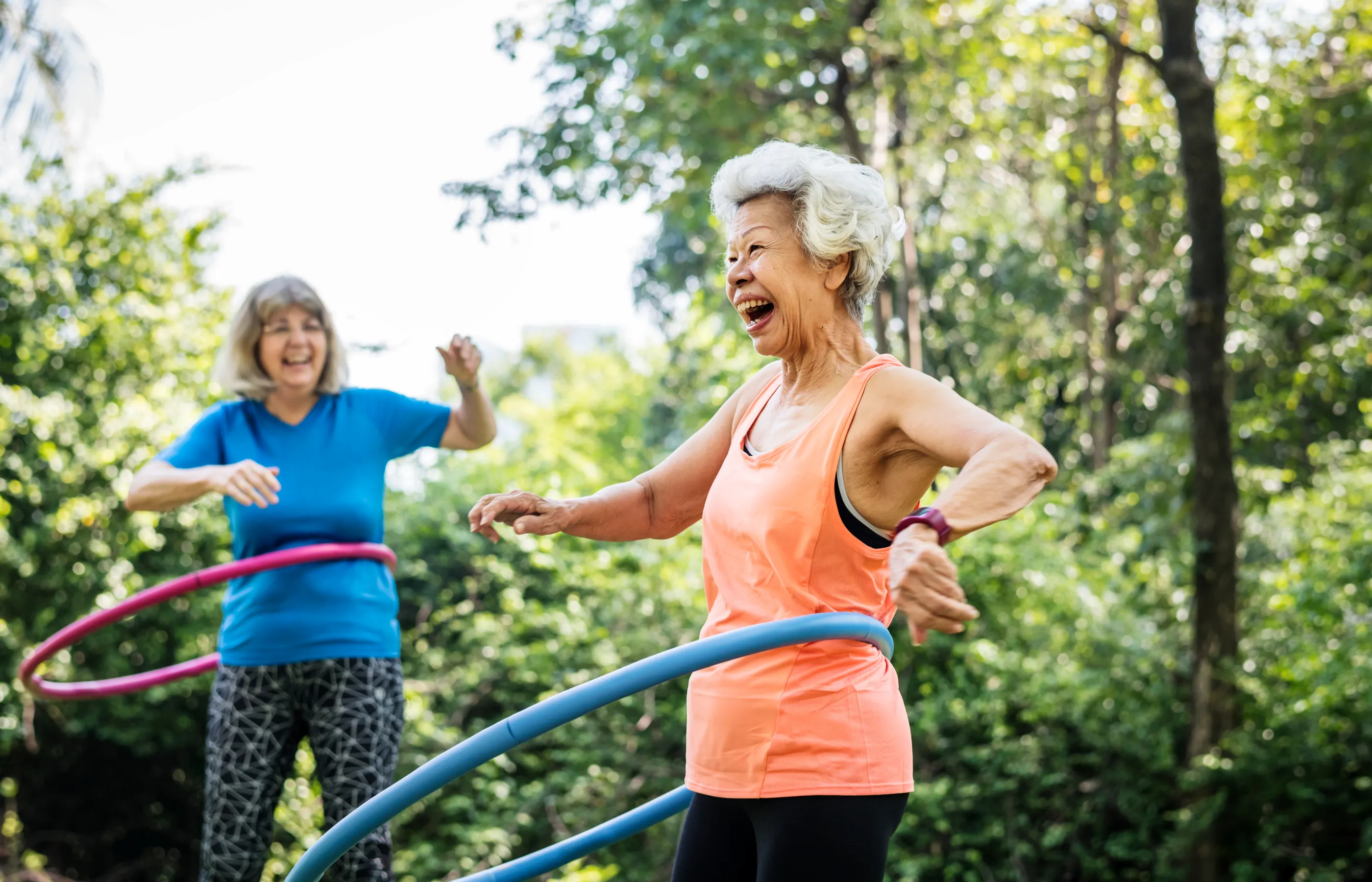 To senior women are outside, having fun, as they use weight hula hoops. 