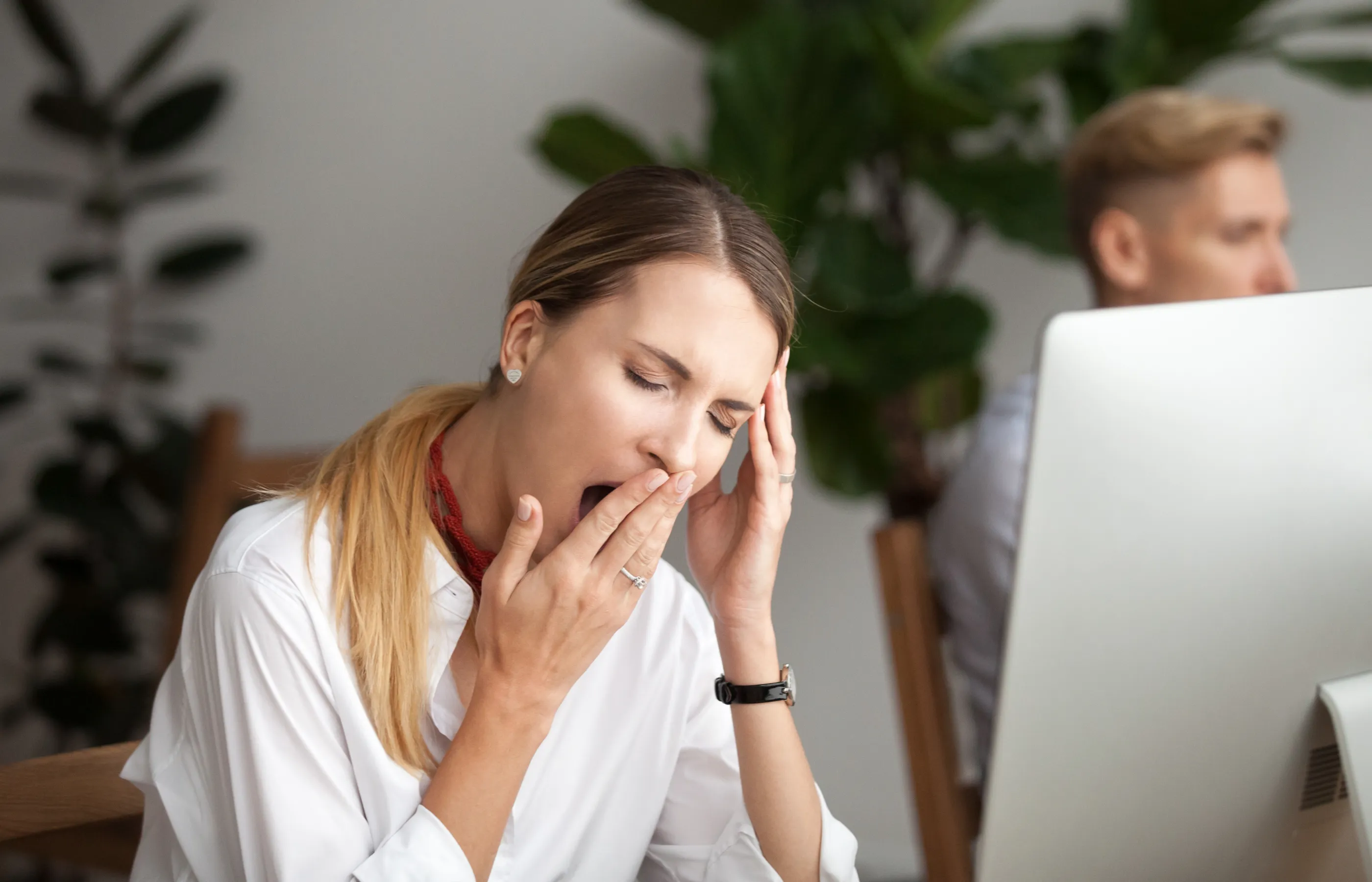 A woman is sitting at her work desk yawning. 