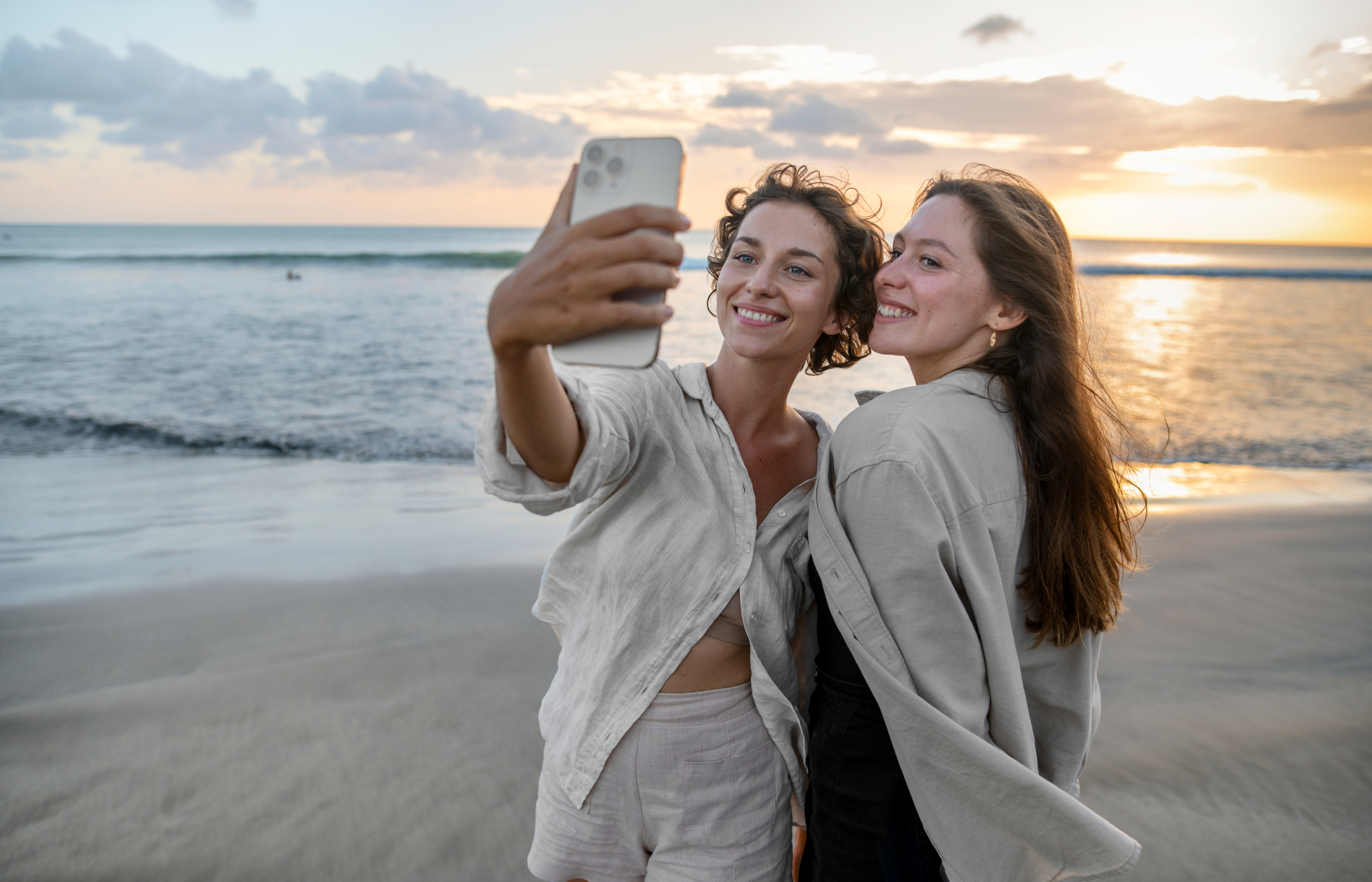 Two women taking a selfie using a smart phone with a sunrise behind them at the beach. Two women taking a selfie using a smart phone with a sunrise behind them at the beach.