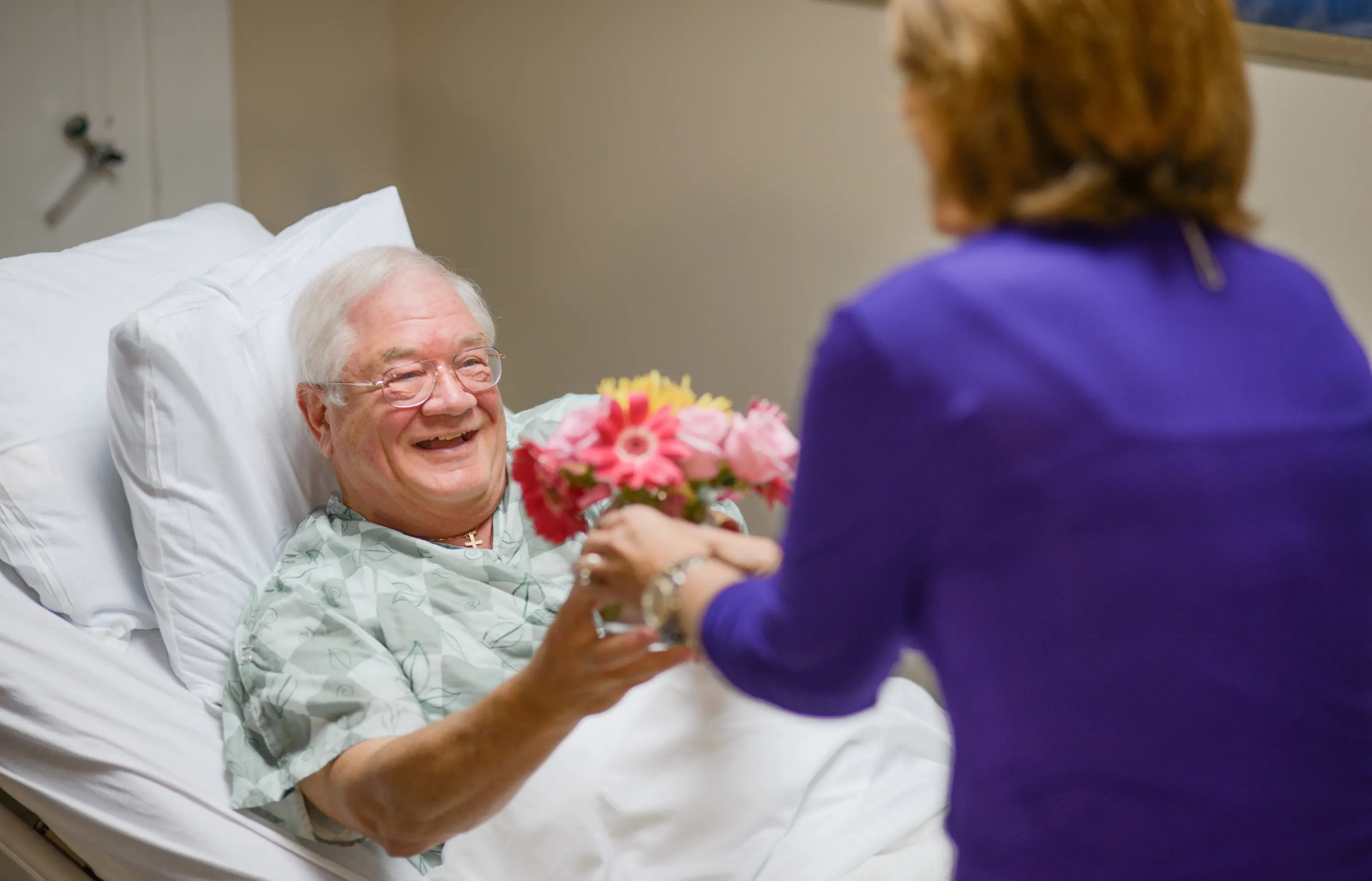 A Novant Health volunteer is delivering flowers to a patient who is lying down in a hospital bed.