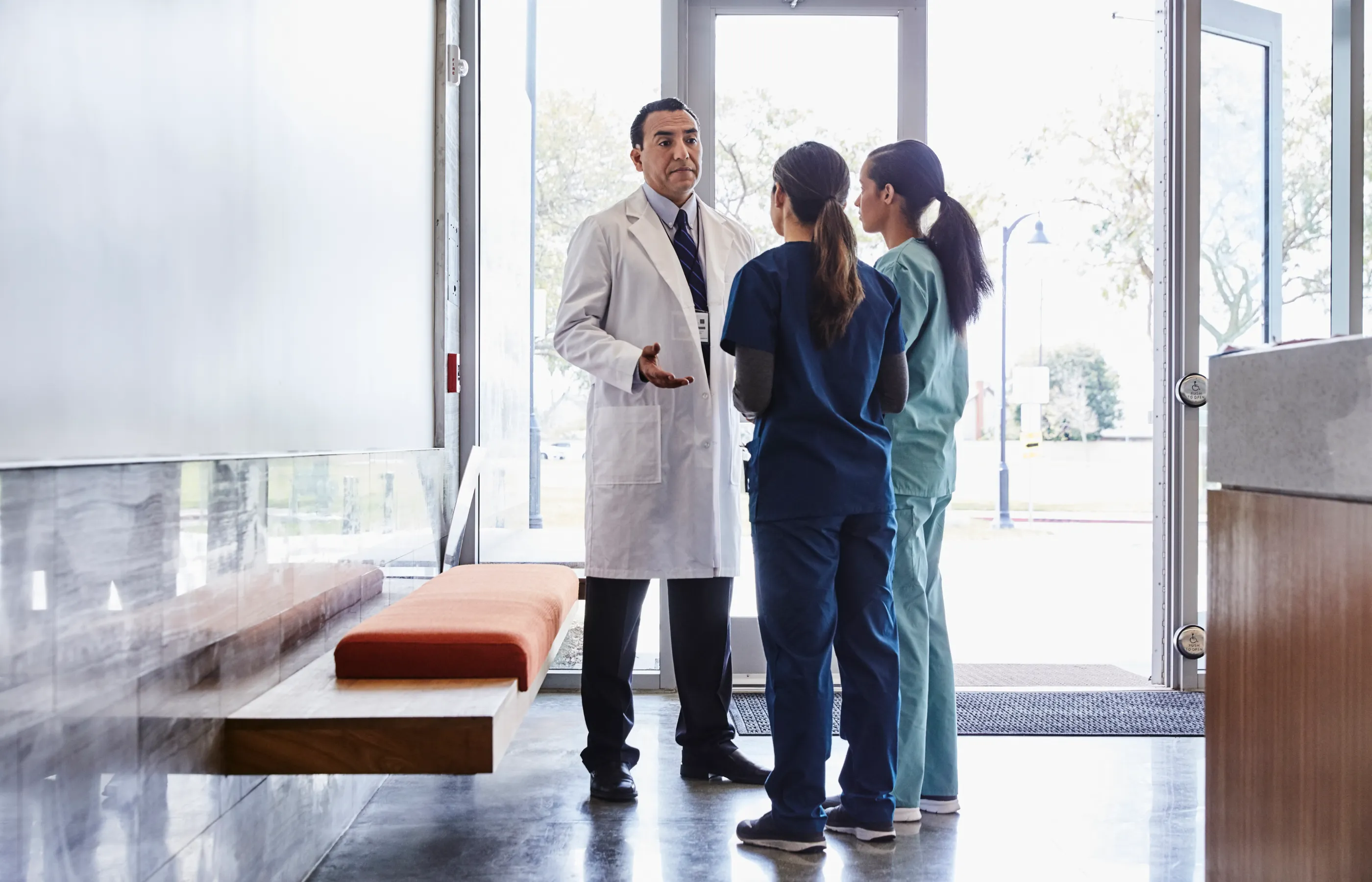 Two women, dressed in scrubs, are talking with a doctor who is wearing a lab coat.  Two women, dressed in scrubs, are talking with a doctor who is wearing a lab coat.
