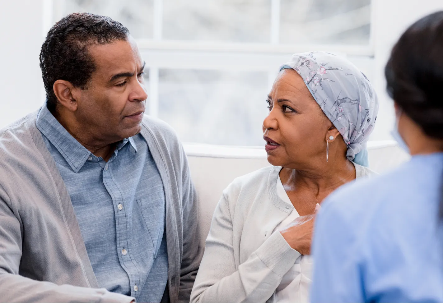 A mature couple is looking at each other and talking as they sit with a nurse. 