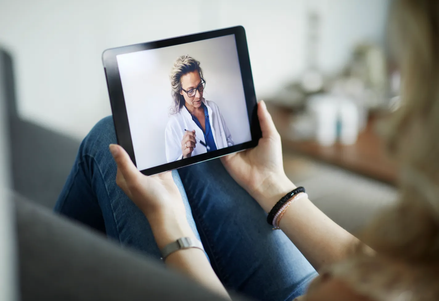 A patient is holding an iPad in their lap with their doctor on the screen during a virtual visit.