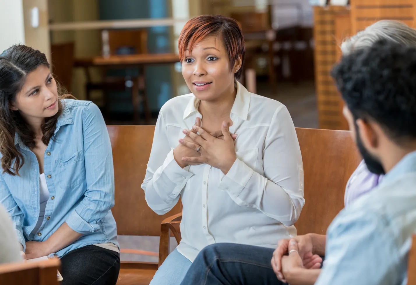 A woman has her hands across her heart as she talks amongst those in her support group. A woman has her hands across her heart as she talks amongst those in her support group.