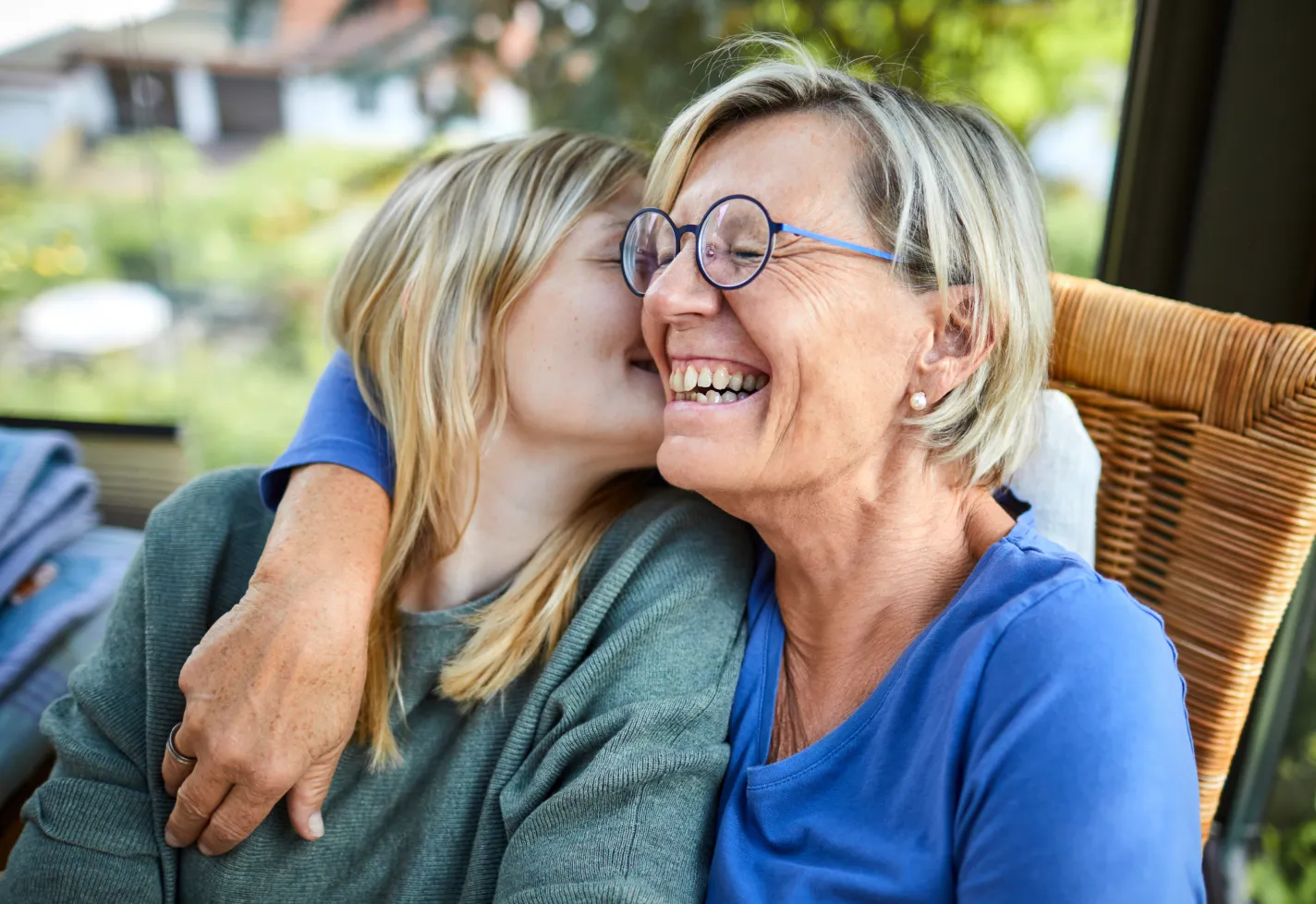 A woman is hugging her adult daughter, as she leans in to kiss her cheek. 