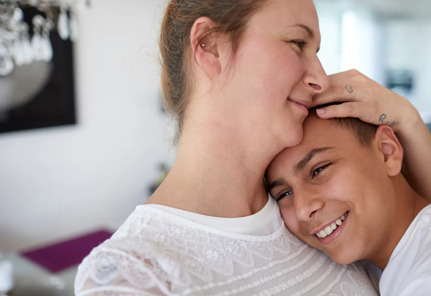 A teenage boy is resting his head on his mothers shoulder as she nestles him. 