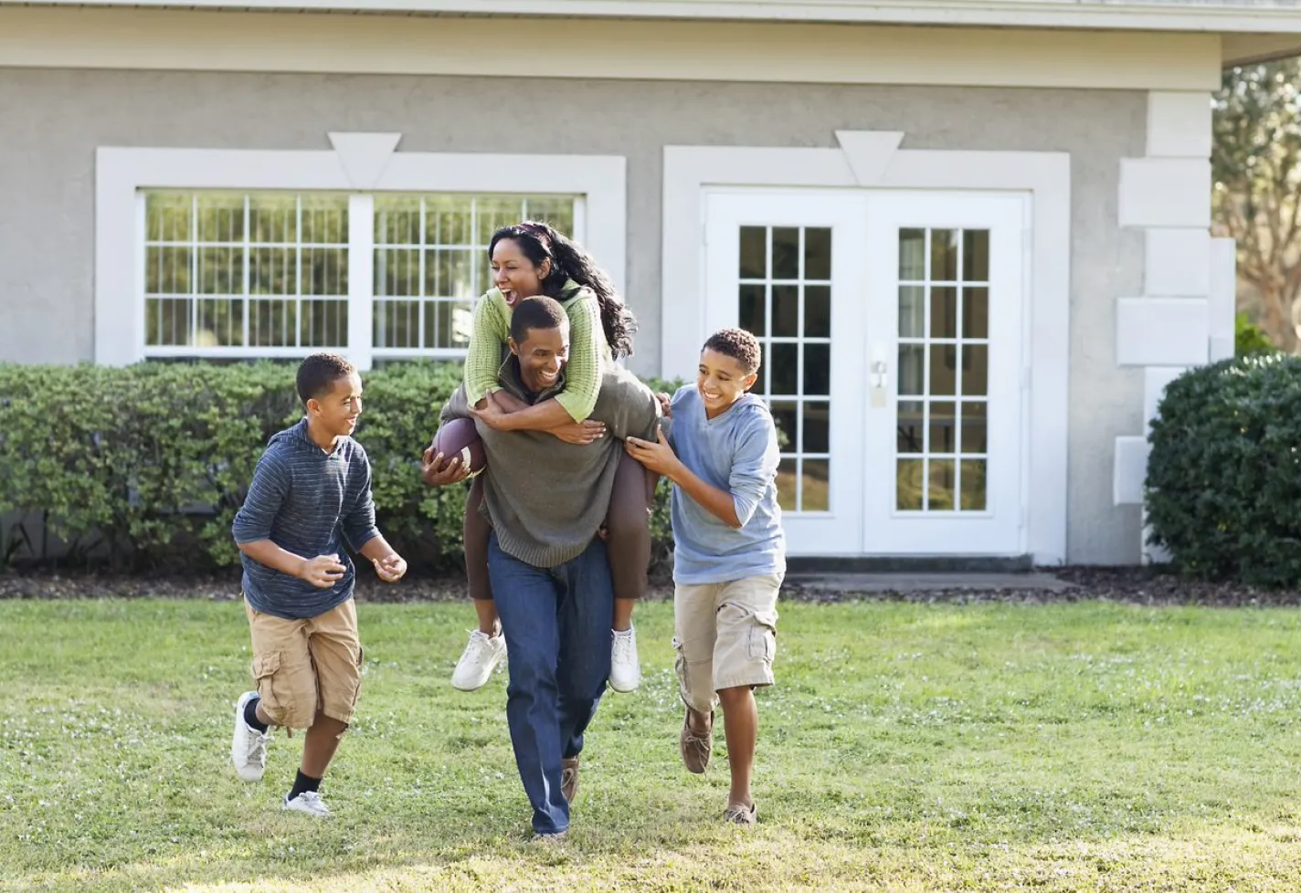 Two children and their parents outside playing and running around with football. 