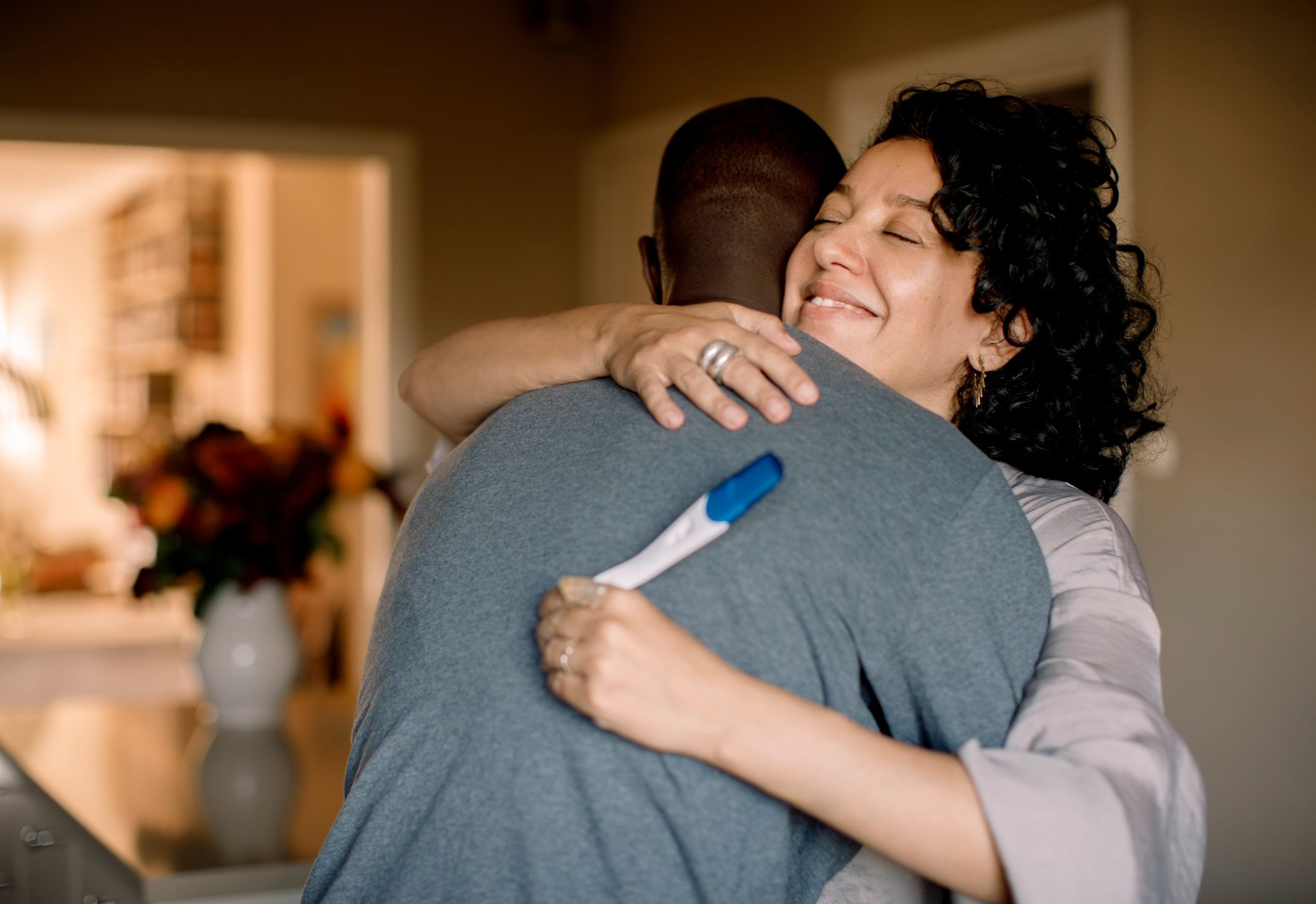 A couple holding a pregnancy test shares a smiling embrace. A couple holding a pregnancy test shares a smiling embrace.
