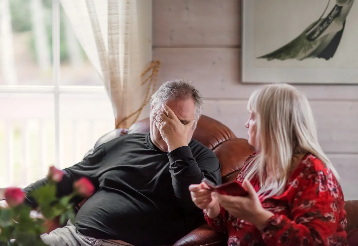 A senior man is sitting in discomfort as his wife calls for medical help. A senior man is sitting in discomfort as his wife calls for medical help.