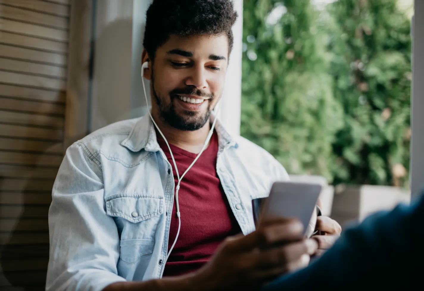 A man is sitting with headphones in and viewing information on his smartphone. 