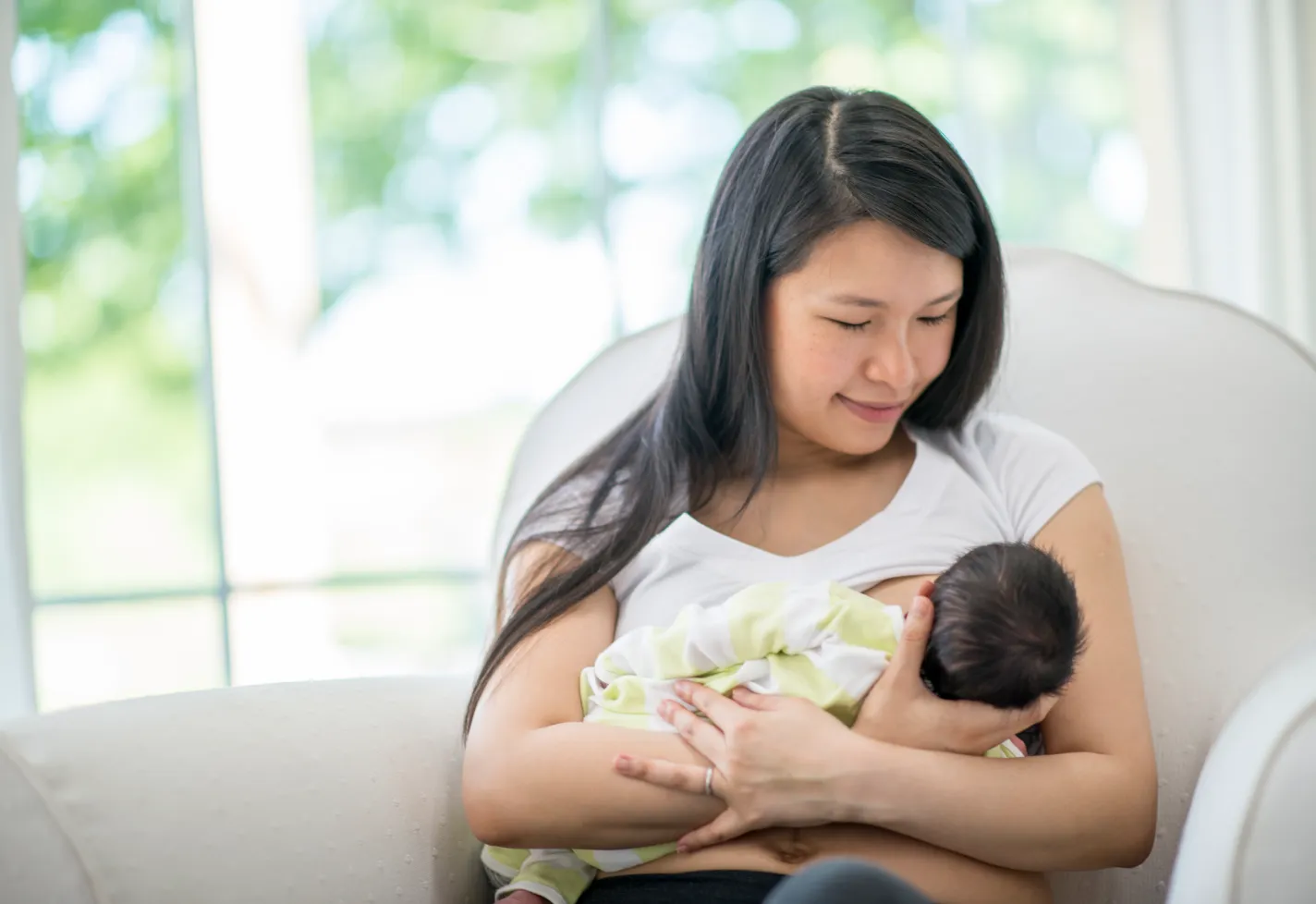A mother breastfeeding hre baby sitting on a chair. A mother breastfeeding hre baby sitting on a chair.