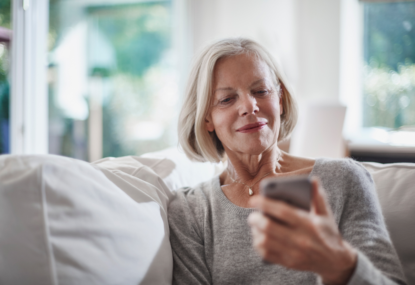 Senior woman sitting on a couch checking a smartphone Senior woman sitting on a couch checking a smartphone
