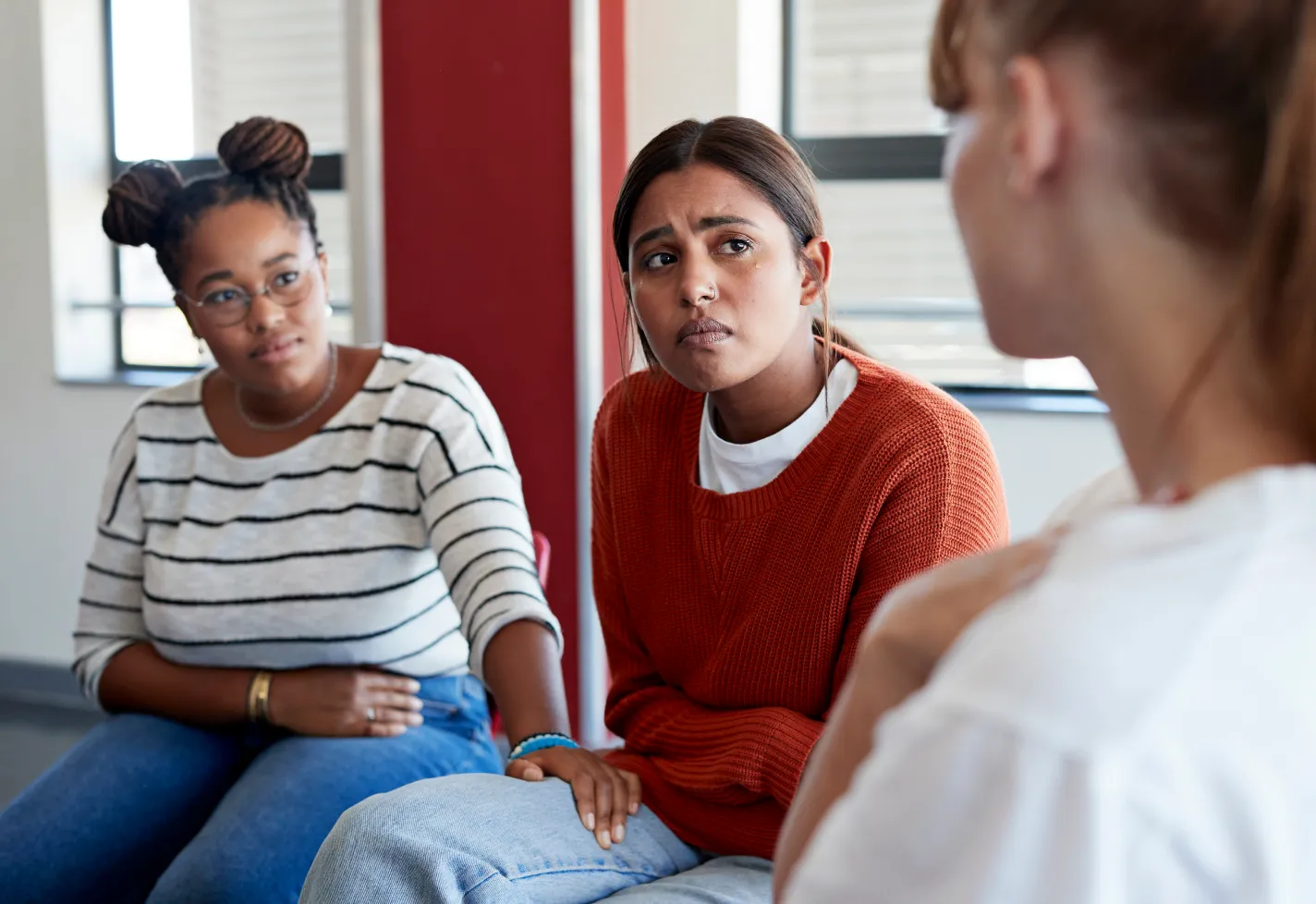 Close-up three multiracial friends in a living room. Woman in the middle is crying and the other two females are giving comfort and support.