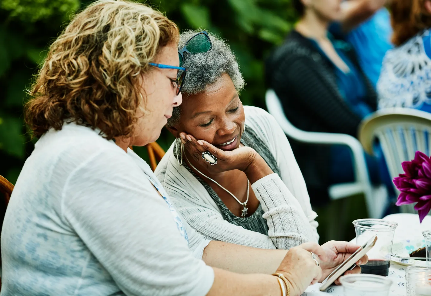 Mature women sitting together, relaxing and looking at a smart phone Mature women sitting together, relaxing and looking at a smart phone