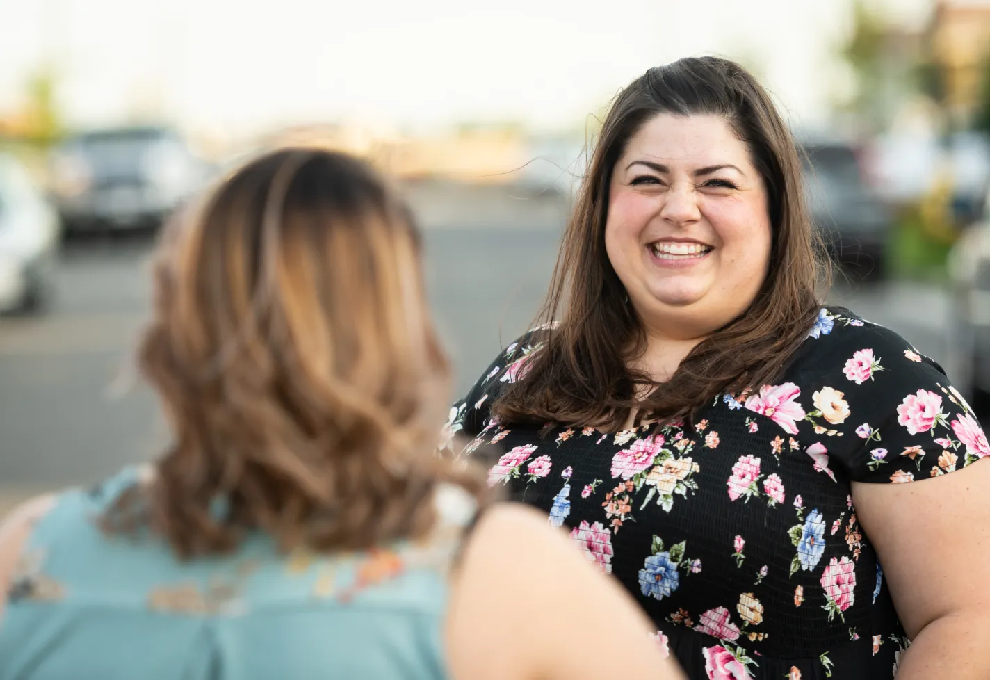 Two women are standing outside talking and smiling at each other. 