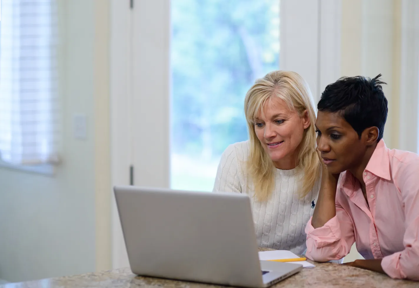 Two woman working on laptop at a kitchen counter 