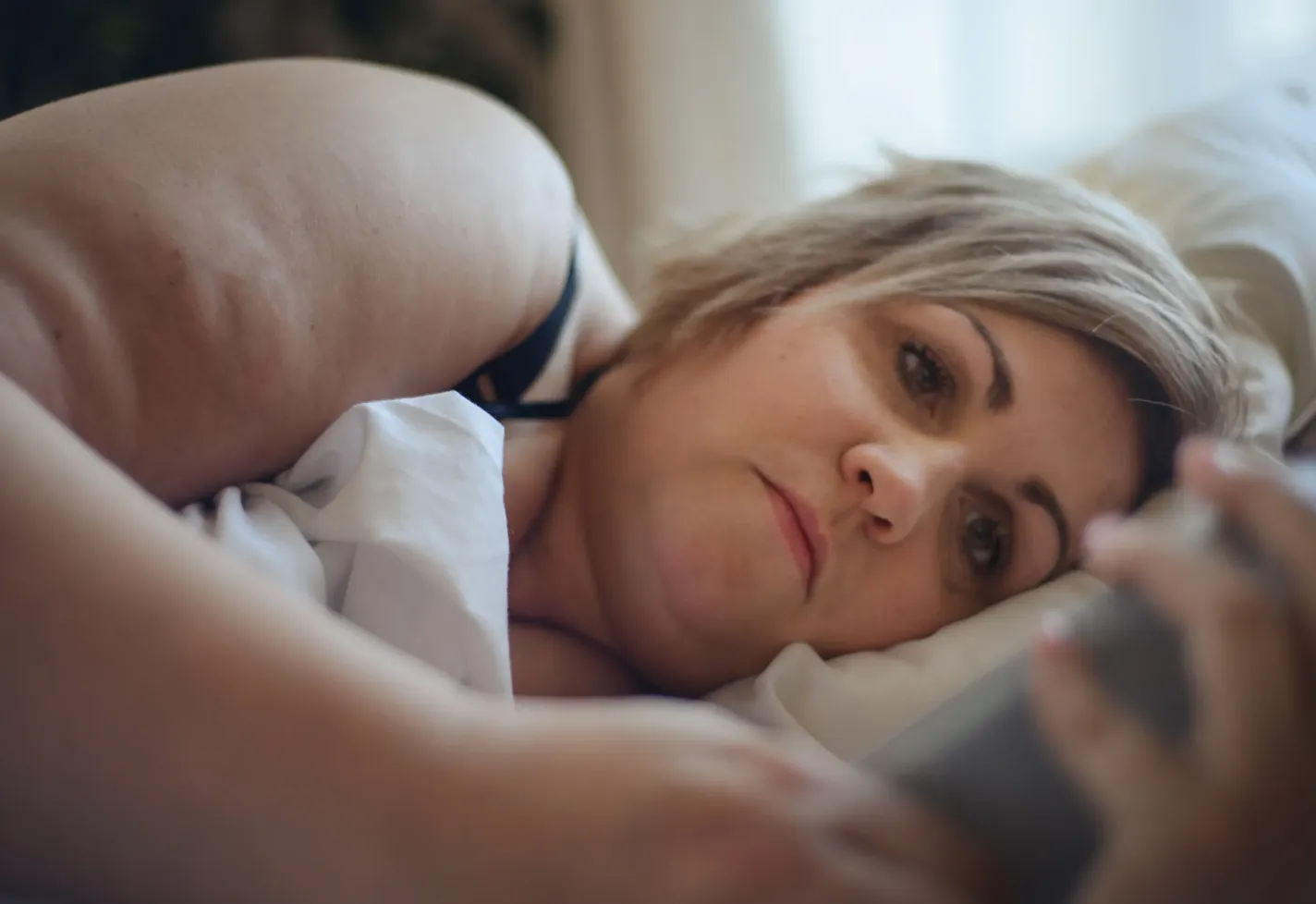 A woman is laying in bed, looking at information on her smartphone. A woman is laying in bed, looking at information on her smartphone.