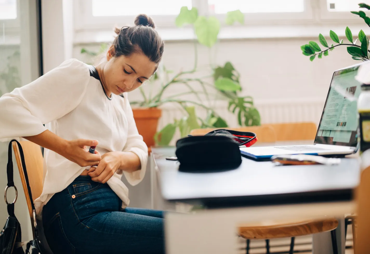 A woman is sitting at a table and preparing to administer and shot in stomach. 