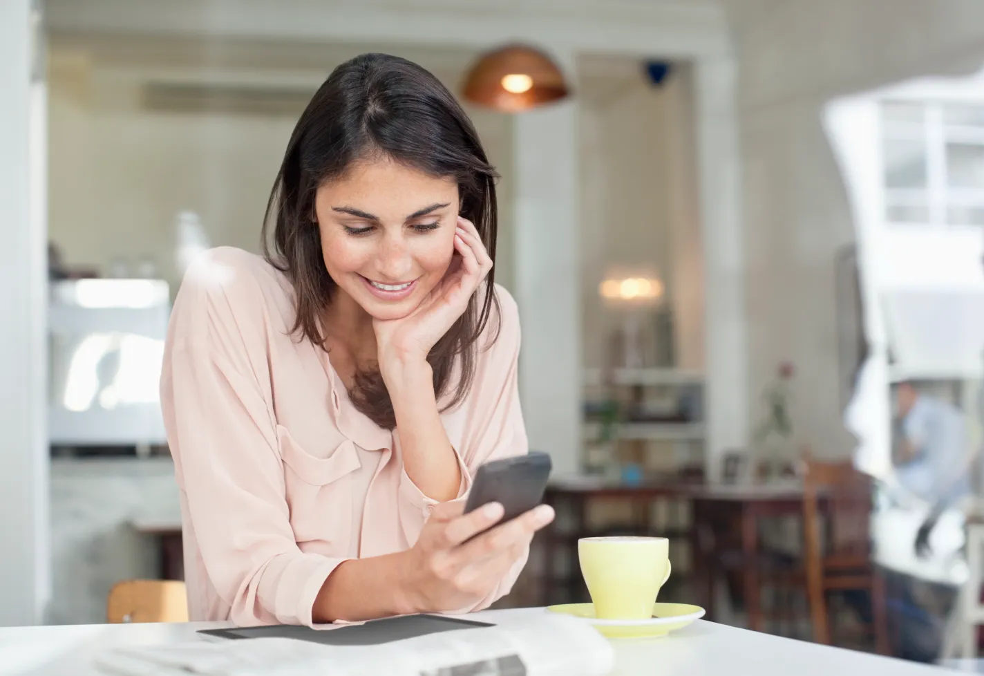 A woman is sitting at a kitchen table viewing information on her phone. A woman is sitting at a kitchen table viewing information on her phone.