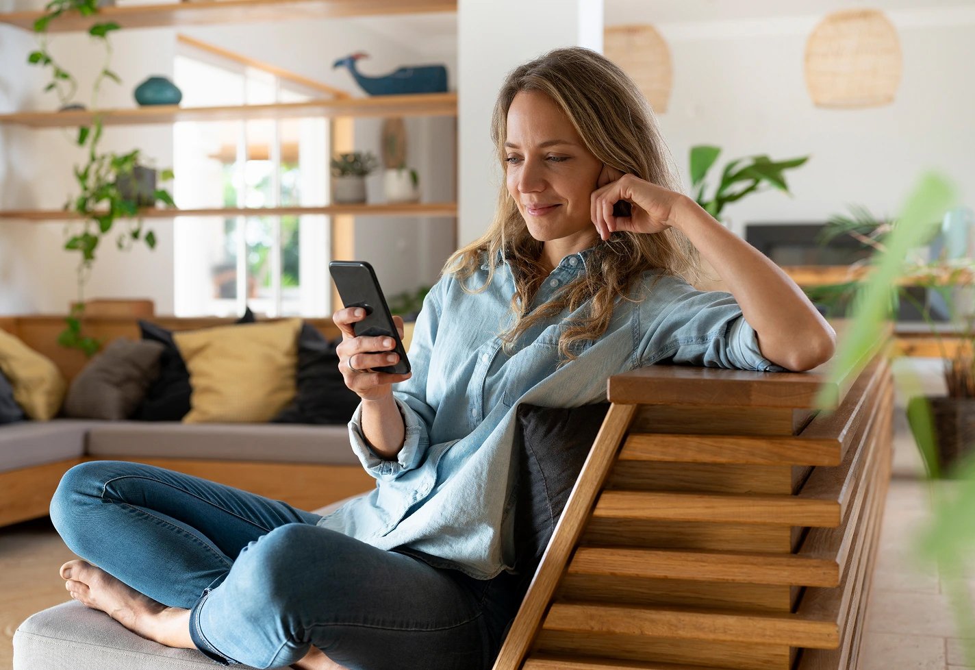 Woman sitting on a wooden couch while looking at her smart phone Woman sitting on a wooden couch while looking at her smart phone