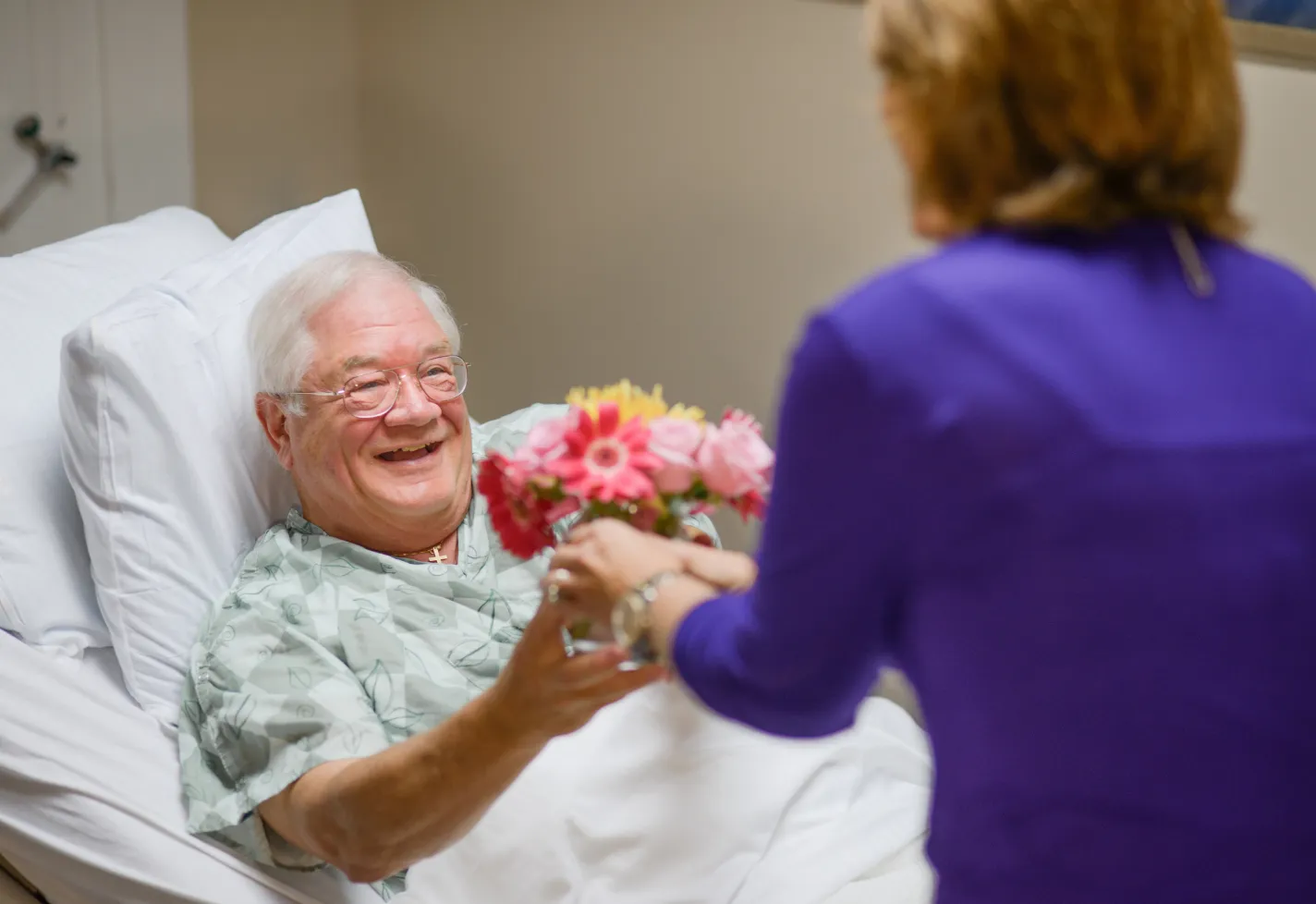A Novant Health volunteer is delivering flowers to a patient who is lying down in a hospital bed. A Novant Health volunteer is delivering flowers to a patient who is lying down in a hospital bed.
