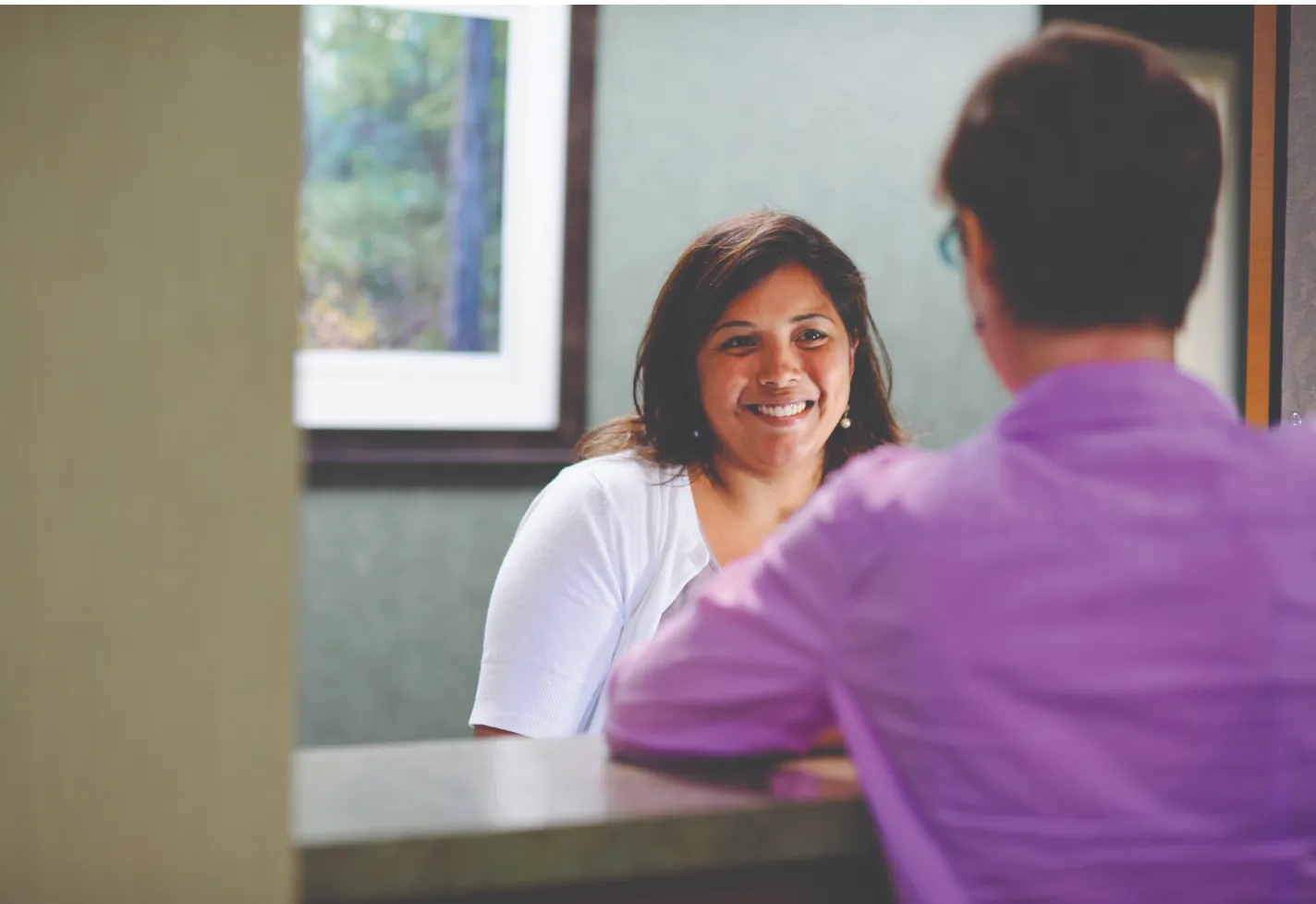 A Novant Health team member is smiling at a patient at the front desk of a clinic. 