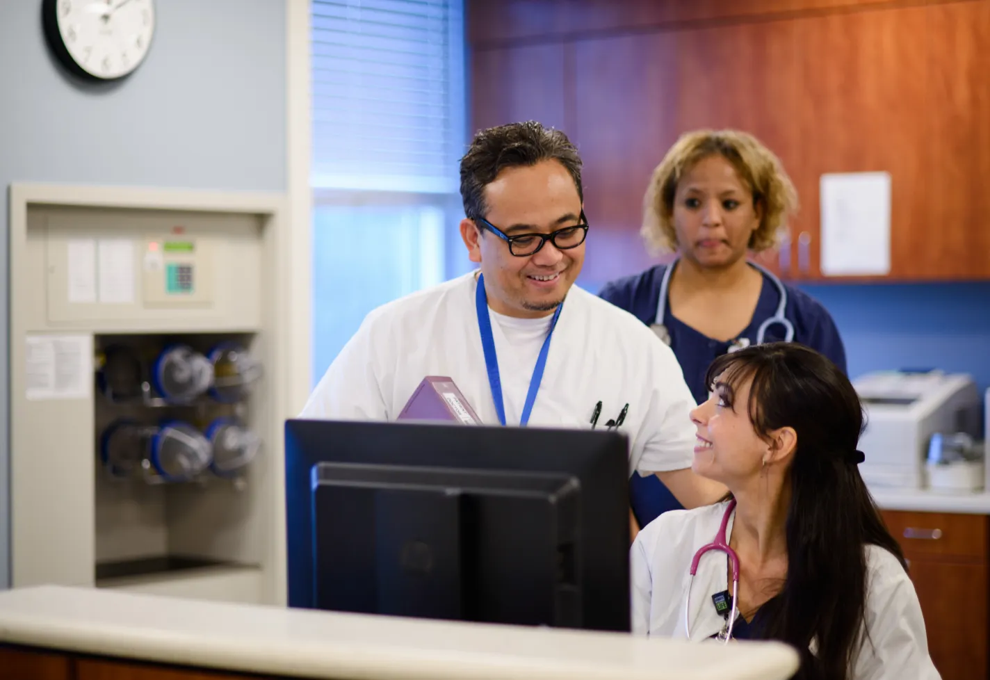 Three Novant Health nurses are at a nurses station talking and smiling. Three Novant Health nurses are at a nurses station talking and smiling.