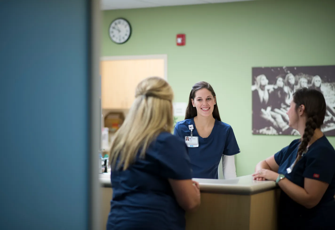 Three Novant Health nurses are talking as they stand around a nurses station. 