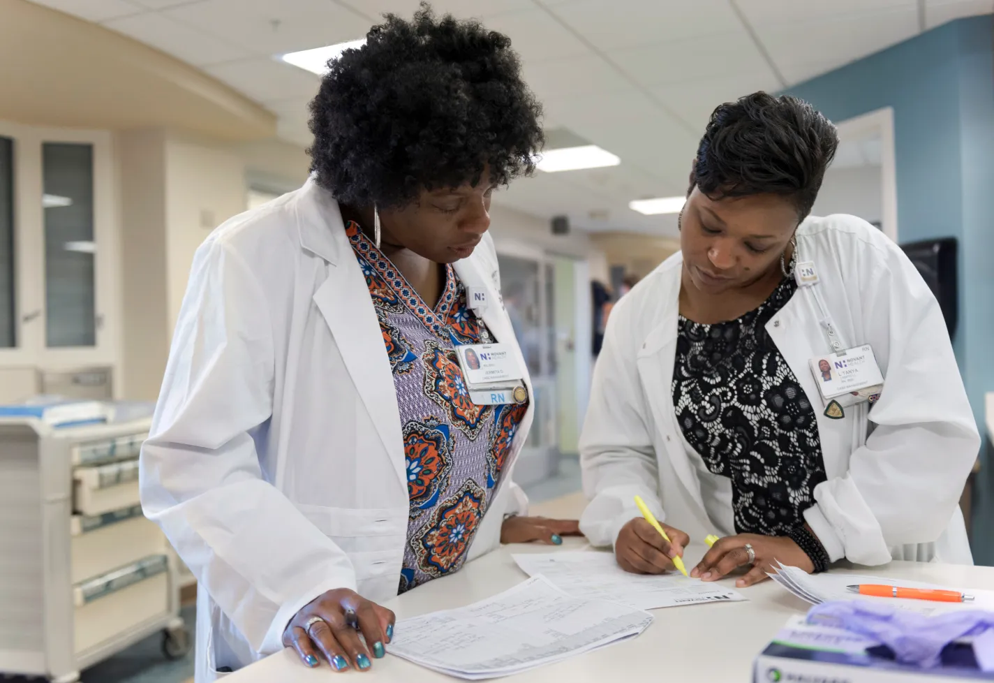 Two Registered Nurses reviewing and filling out forms at a counter in the hospital. 